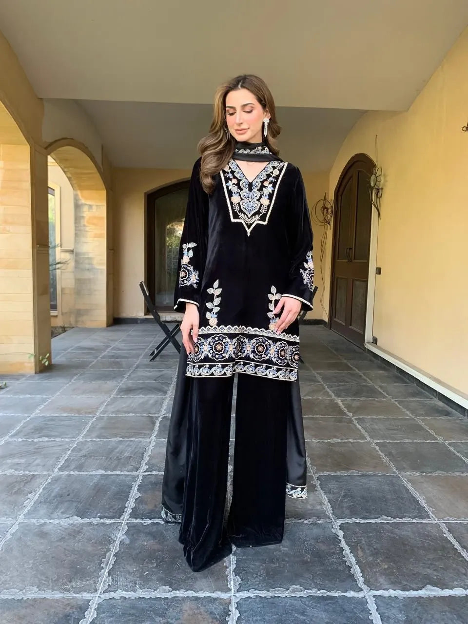 Woman wearing a black outfit with white embroidery standing in an outdoor setting.