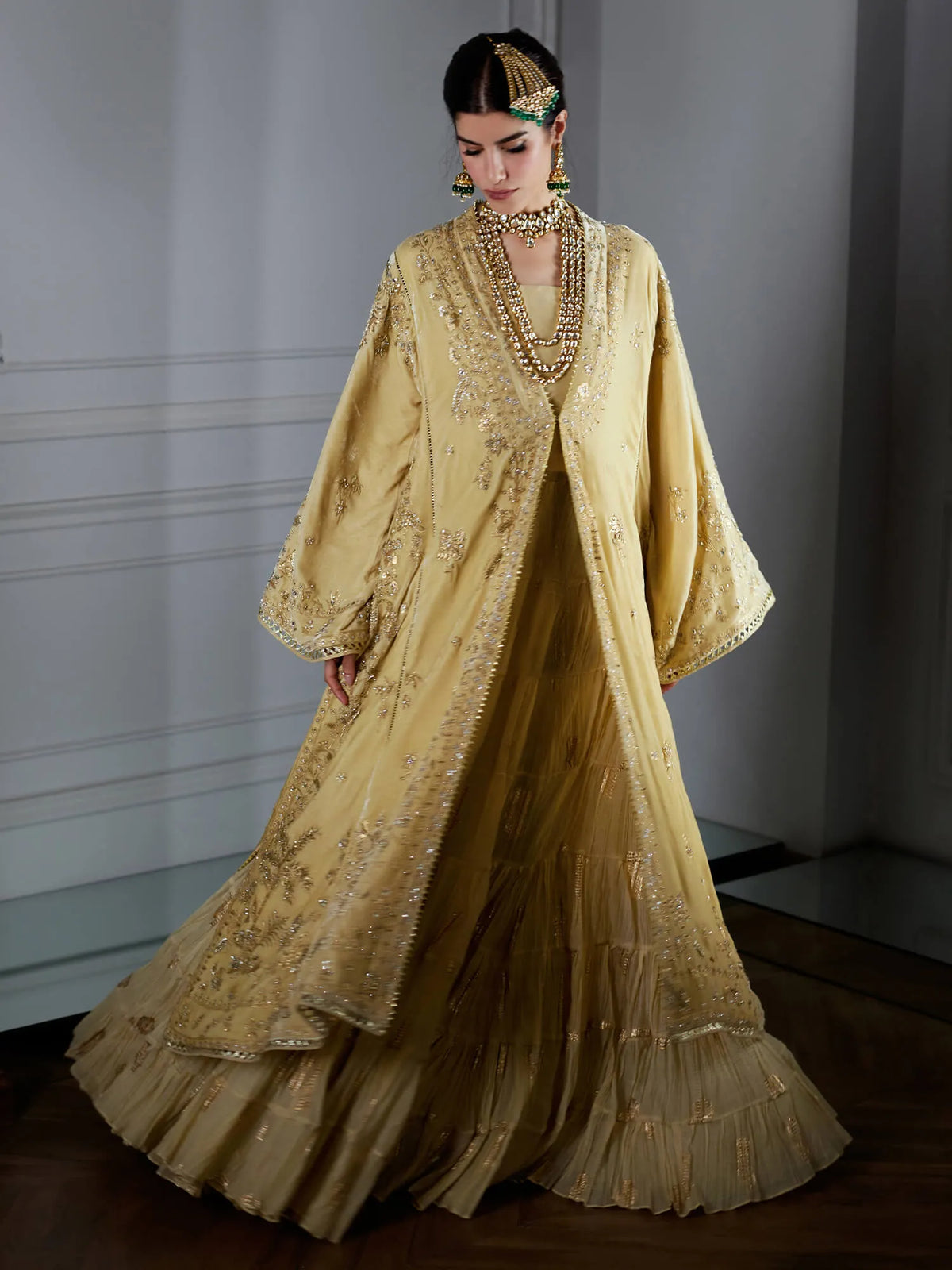 Woman wearing a long, elegant gold dress with intricate detailing in a minimalistic setting.