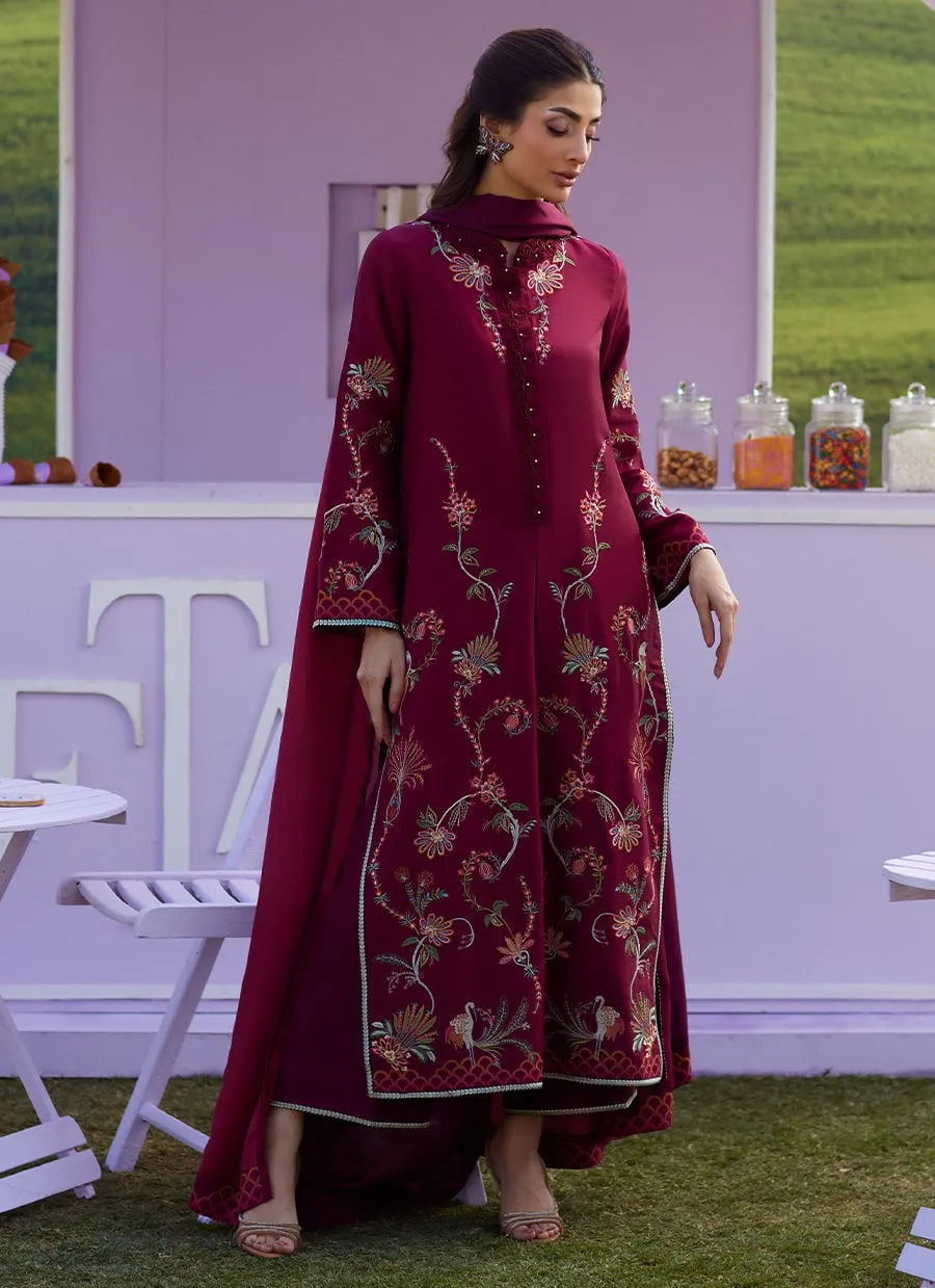 Woman in a burgundy embroidered dress standing outdoors with a display of jars in the background.