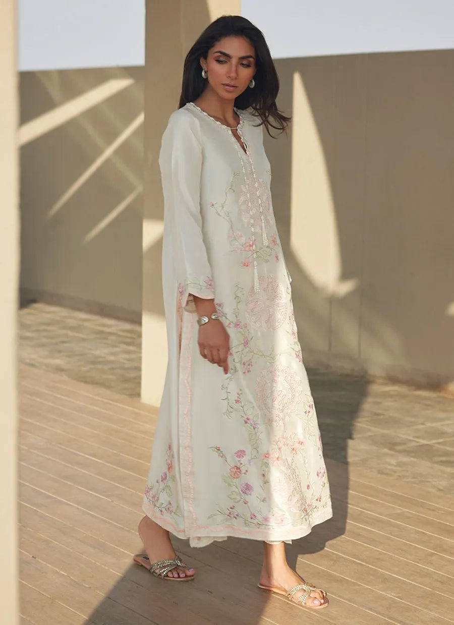 Woman wearing a light-colored floral dress standing in a sunlit outdoor setting.