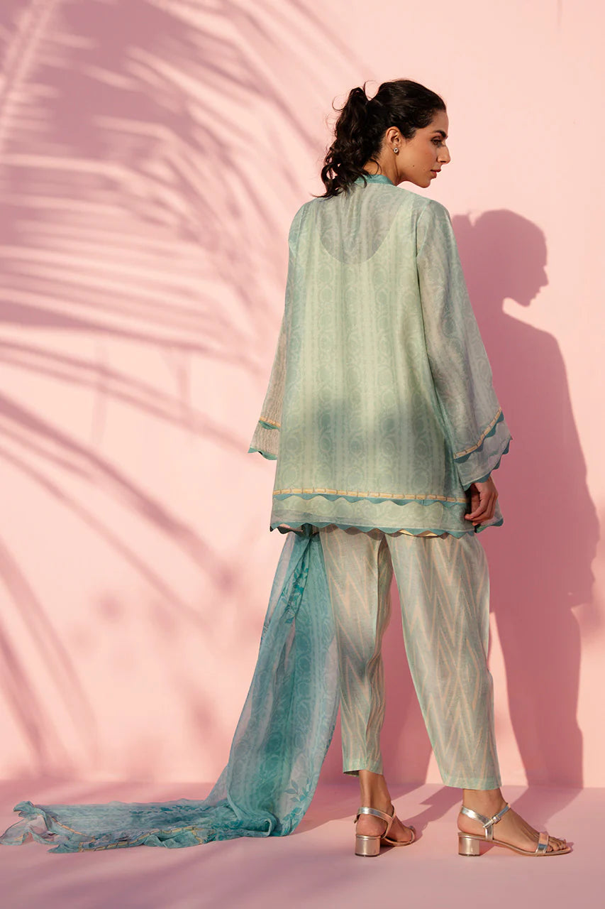 Woman in a light green traditional outfit with a pink background