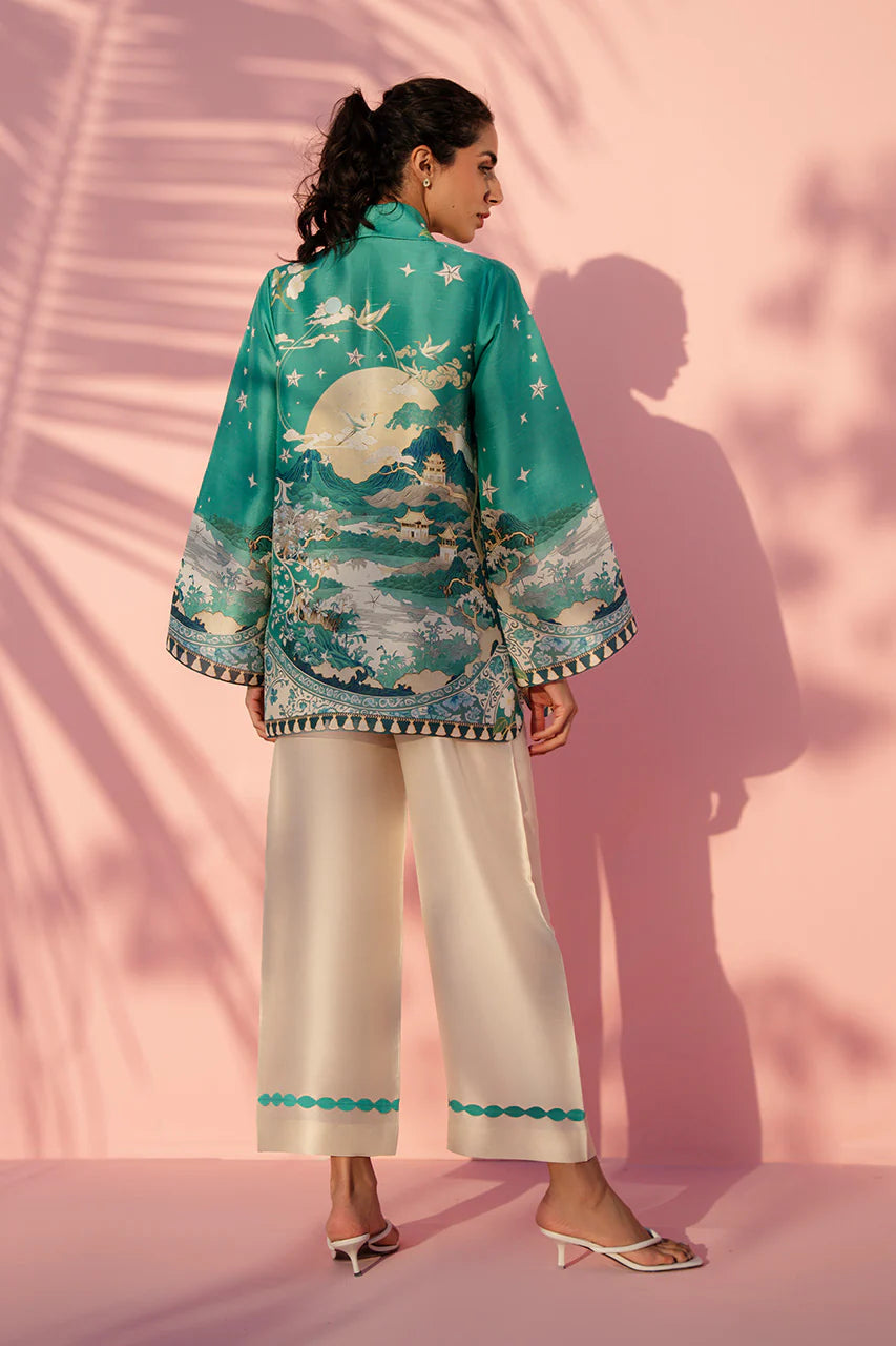 Woman wearing a teal embroidered jacket and white pants against a pink background