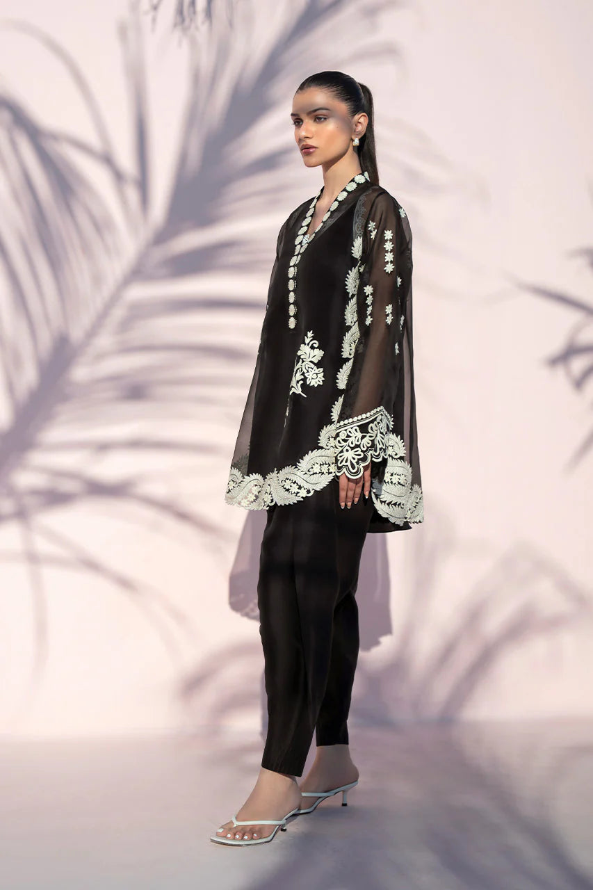 Woman wearing a black outfit with white lace details against a neutral background