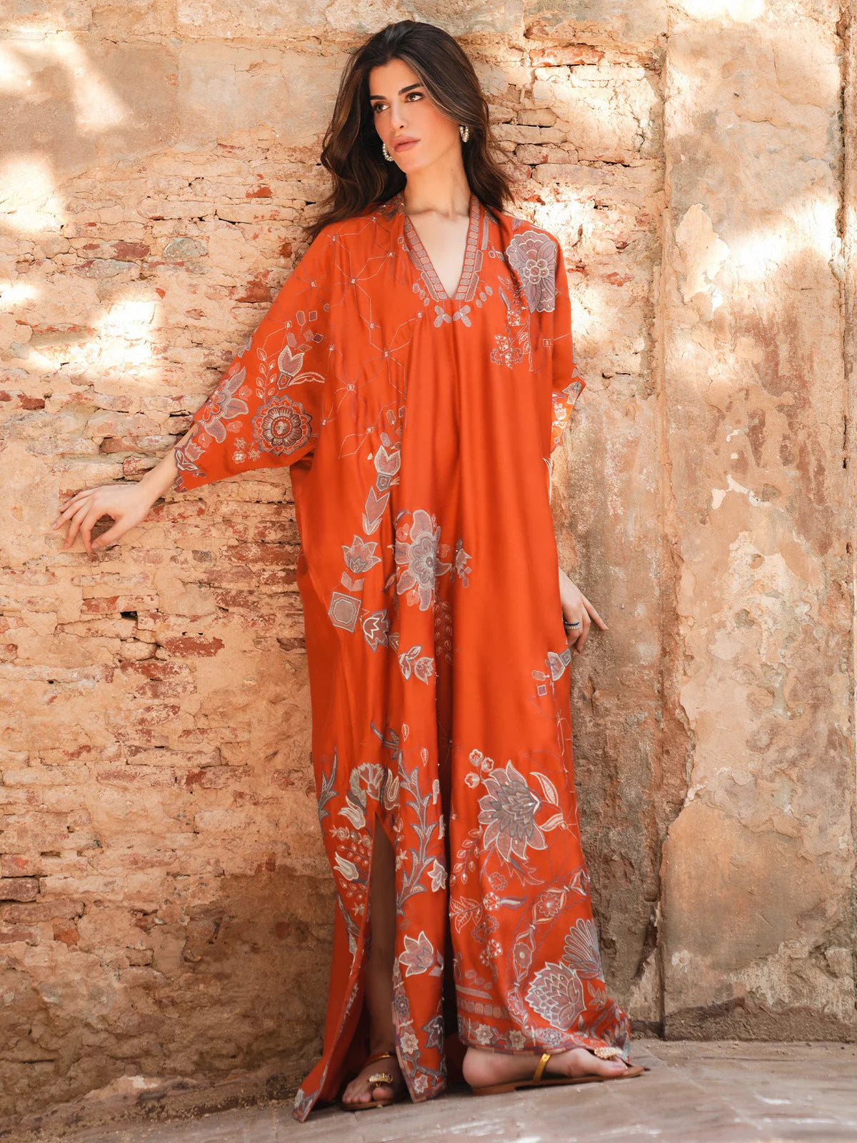Woman wearing an orange embroidered outfit against a textured stone wall.