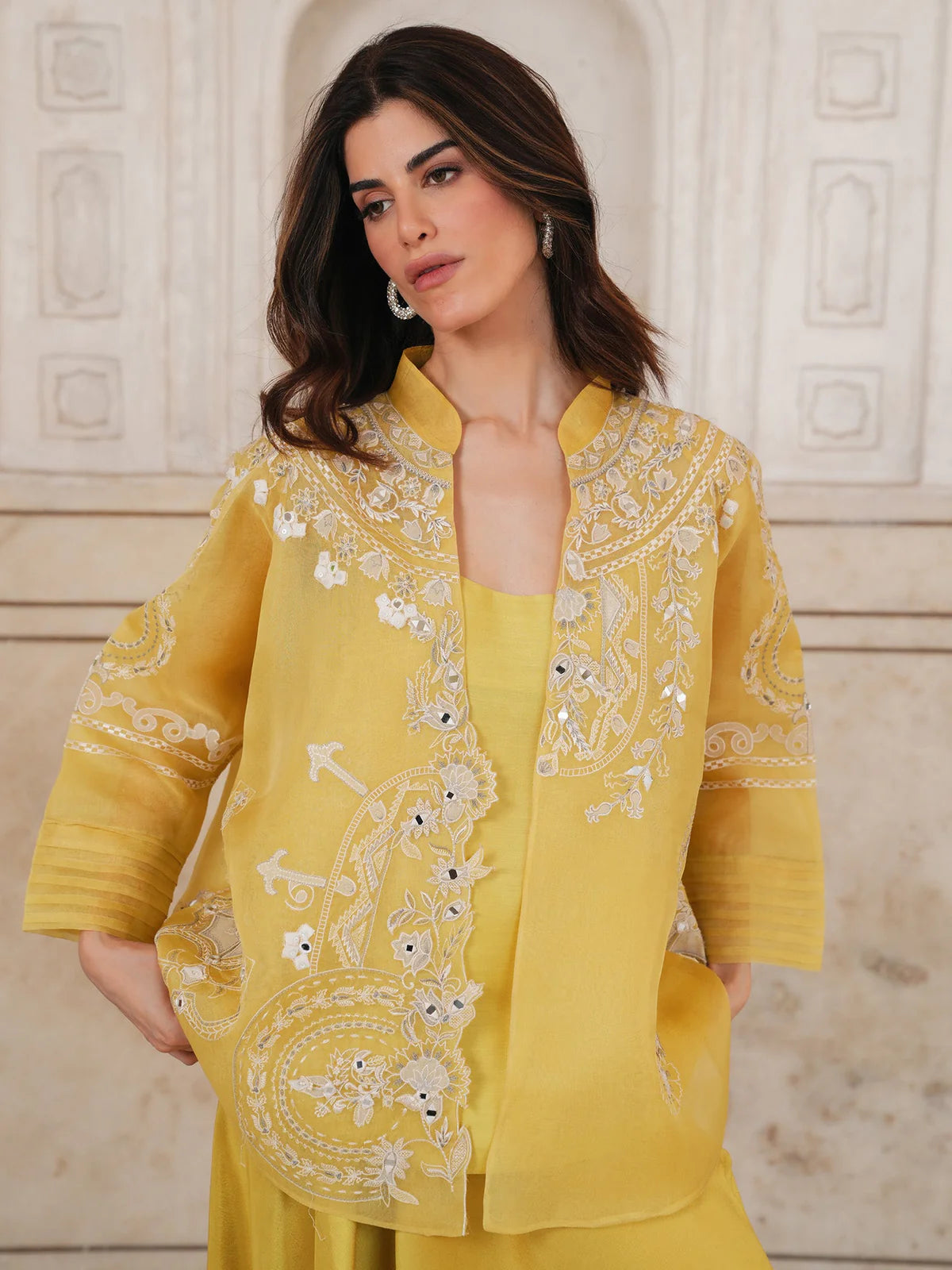 Woman wearing a yellow embroidered outfit against a decorative wall.