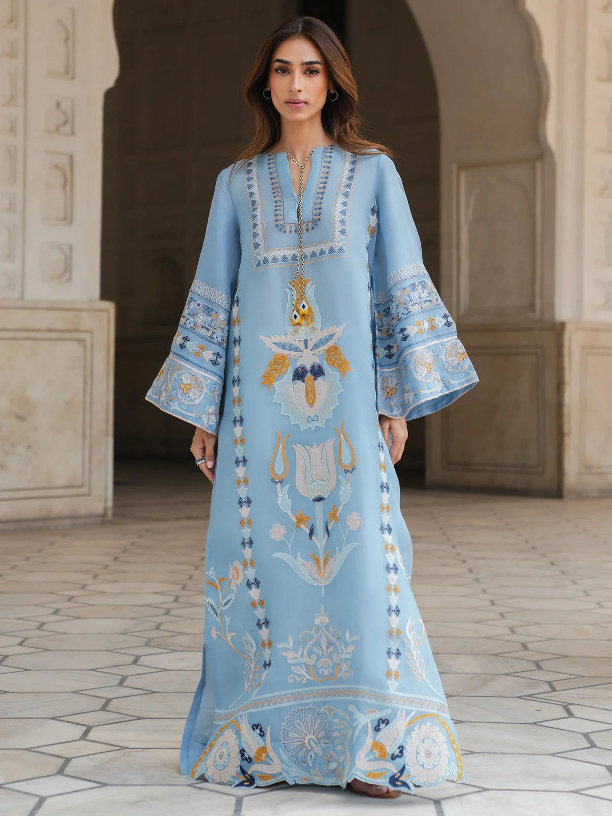 Woman wearing a light blue embroidered dress standing in front of an archway.