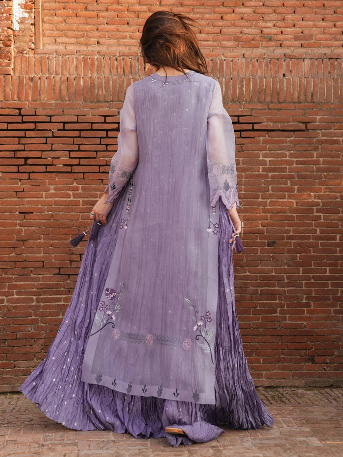 Person wearing a long, light purple embroidered dress against a brick wall.