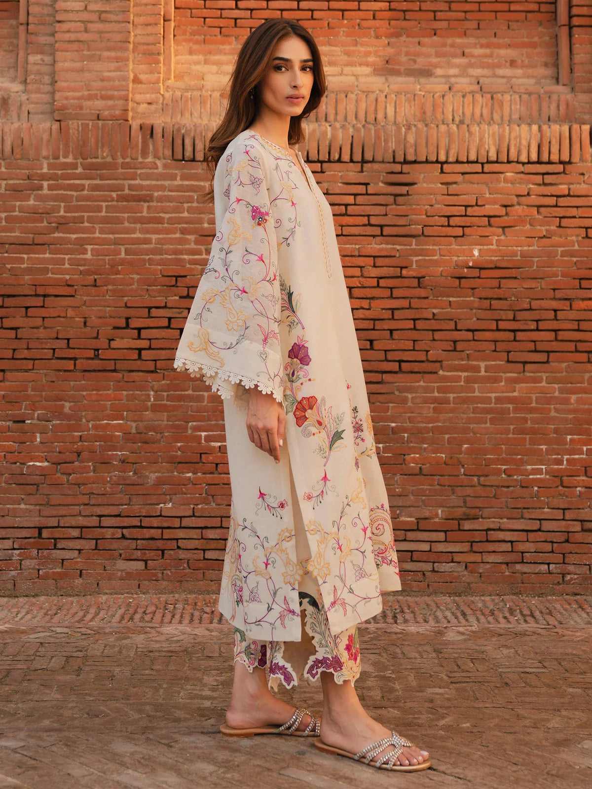 Woman wearing a floral dress standing against a brick wall.