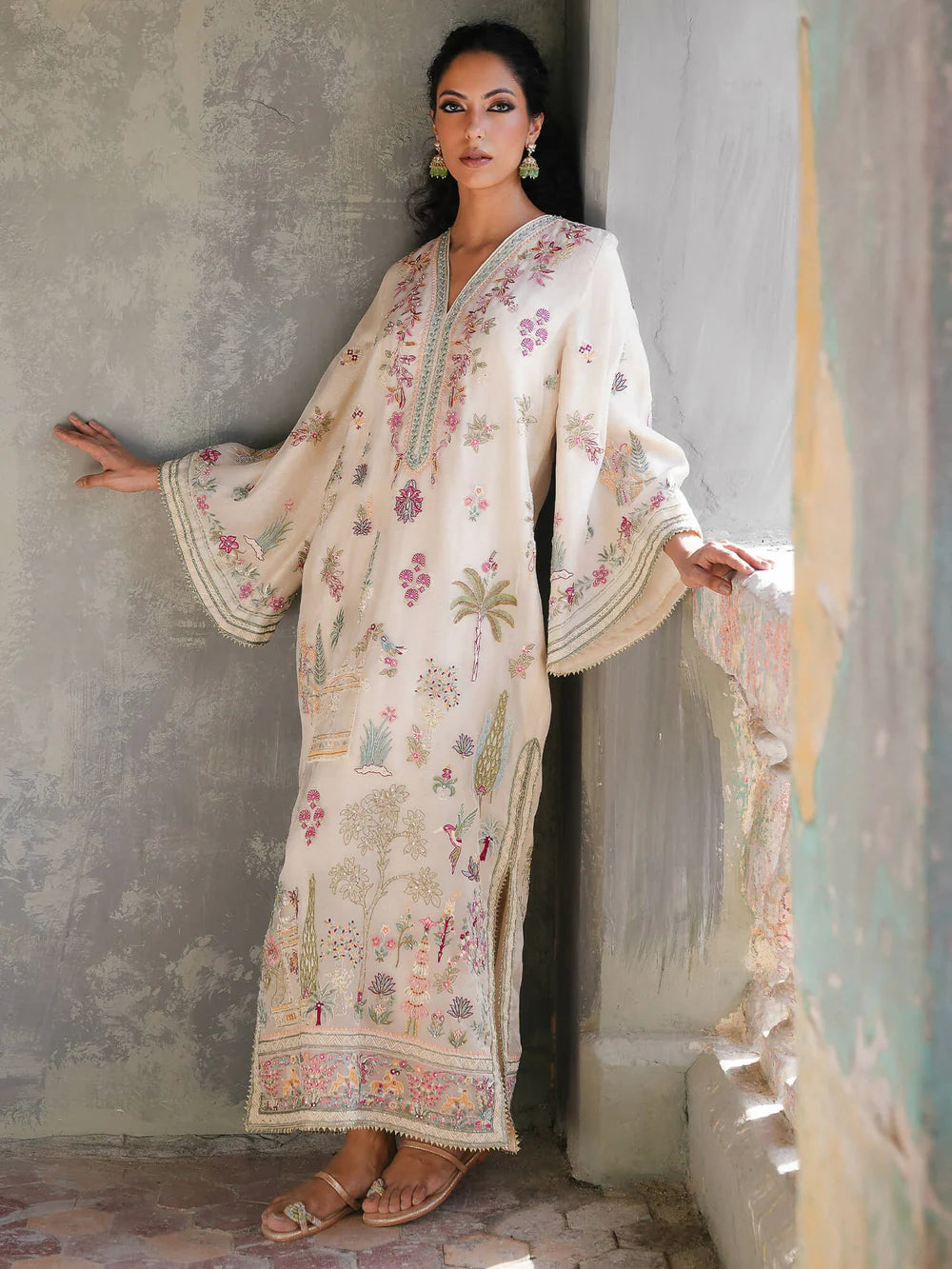 Woman wearing a floral embroidered dress against a textured wall.