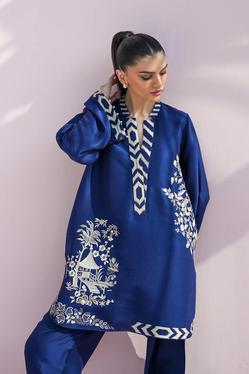 Woman wearing a blue embroidered traditional outfit against a white background