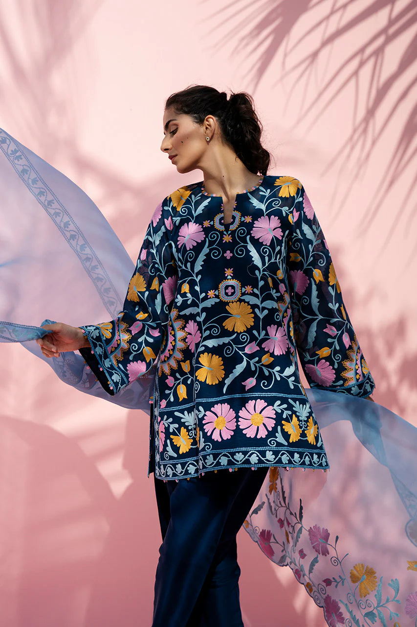 Woman wearing a colorful floral embroidered top against a pink background
