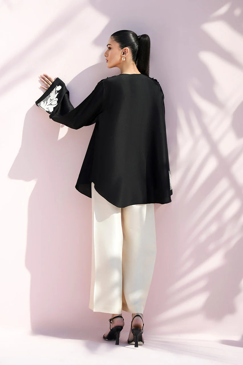 Woman wearing a black outfit with white pants against a light pink wall