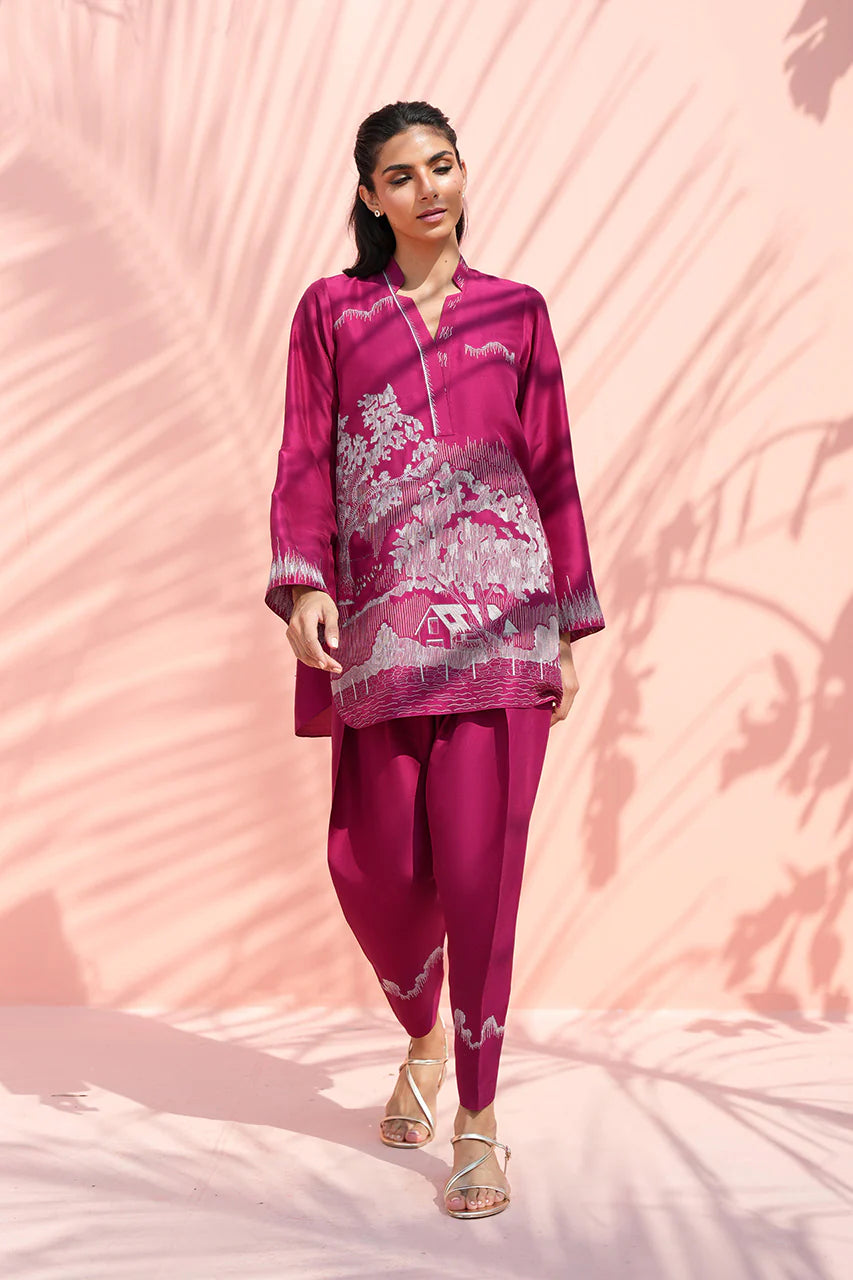Woman wearing a magenta traditional outfit with white patterns against a pink background