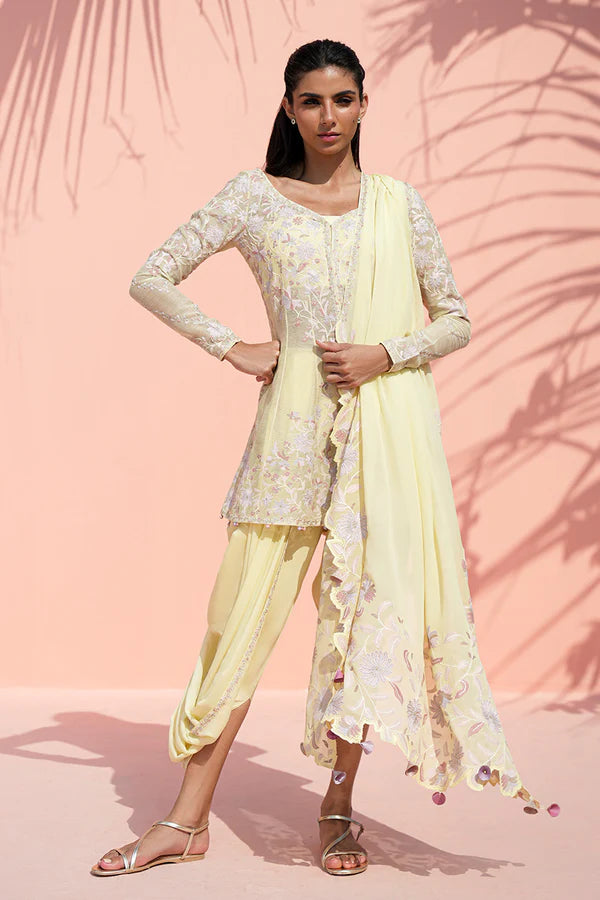 Woman in a light yellow traditional outfit with floral patterns against a pink background