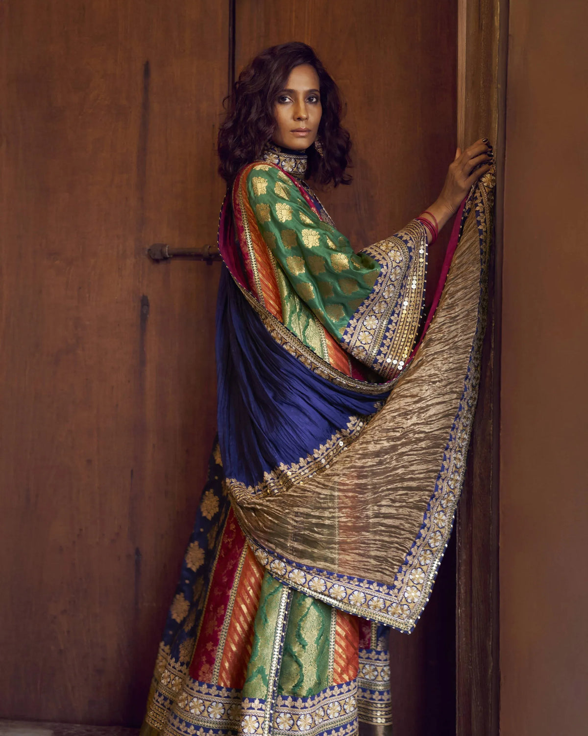 Woman in traditional embroidered outfit sitting in a doorway in standing pose.