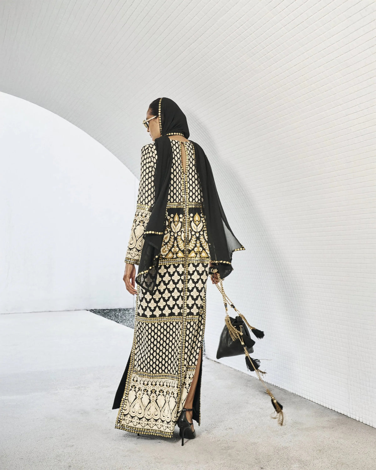 Woman in a black and gold traditional outfit with a matching headscarf, standing against a white background.