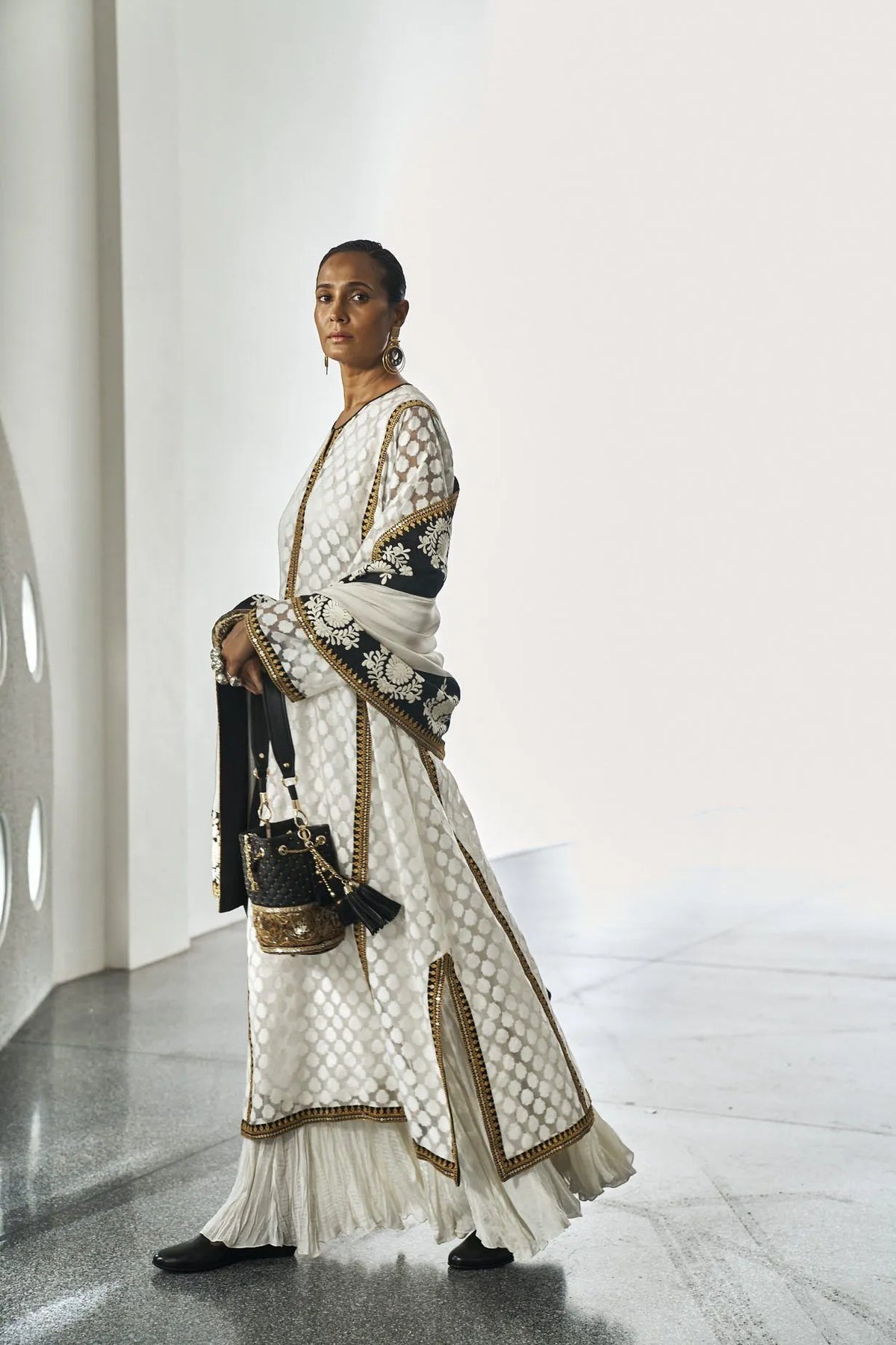 Woman in a white and black patterned dress holding a black handbag in a modern indoor setting.