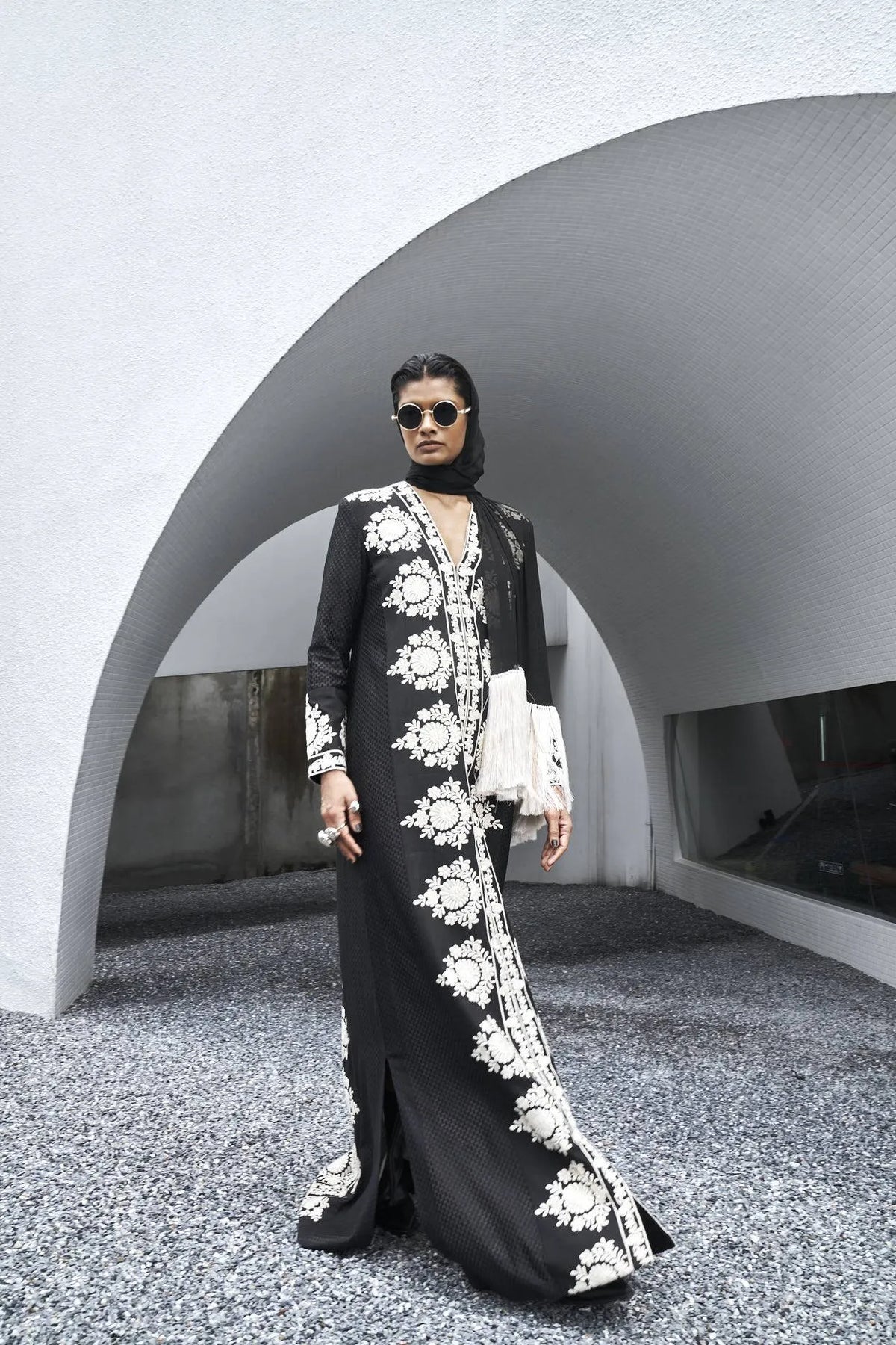 Woman in a black and white embroidered dress standing in front of a modern architectural structure.