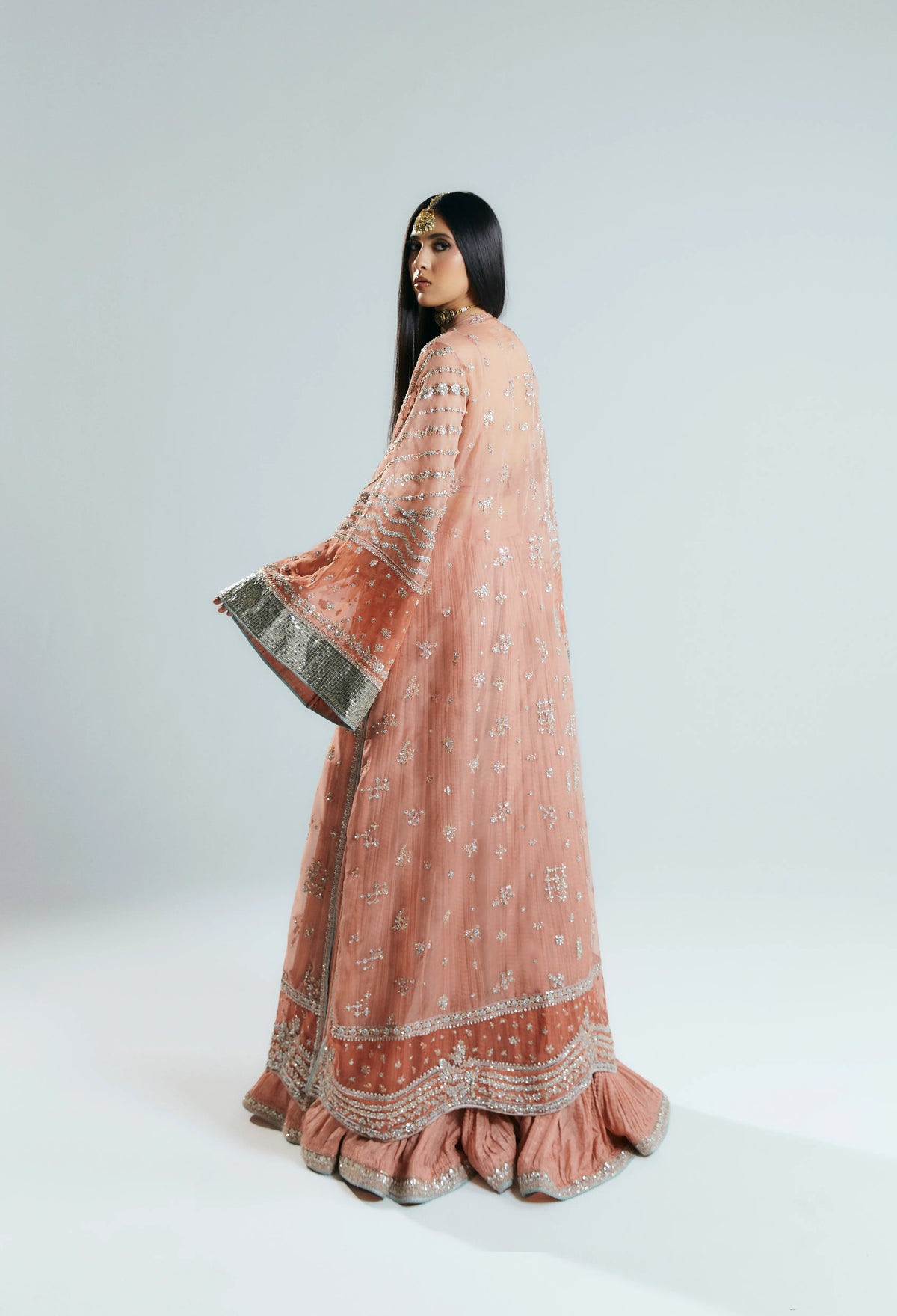 Woman wearing a traditional pink and orange embroidered outfit on a white background