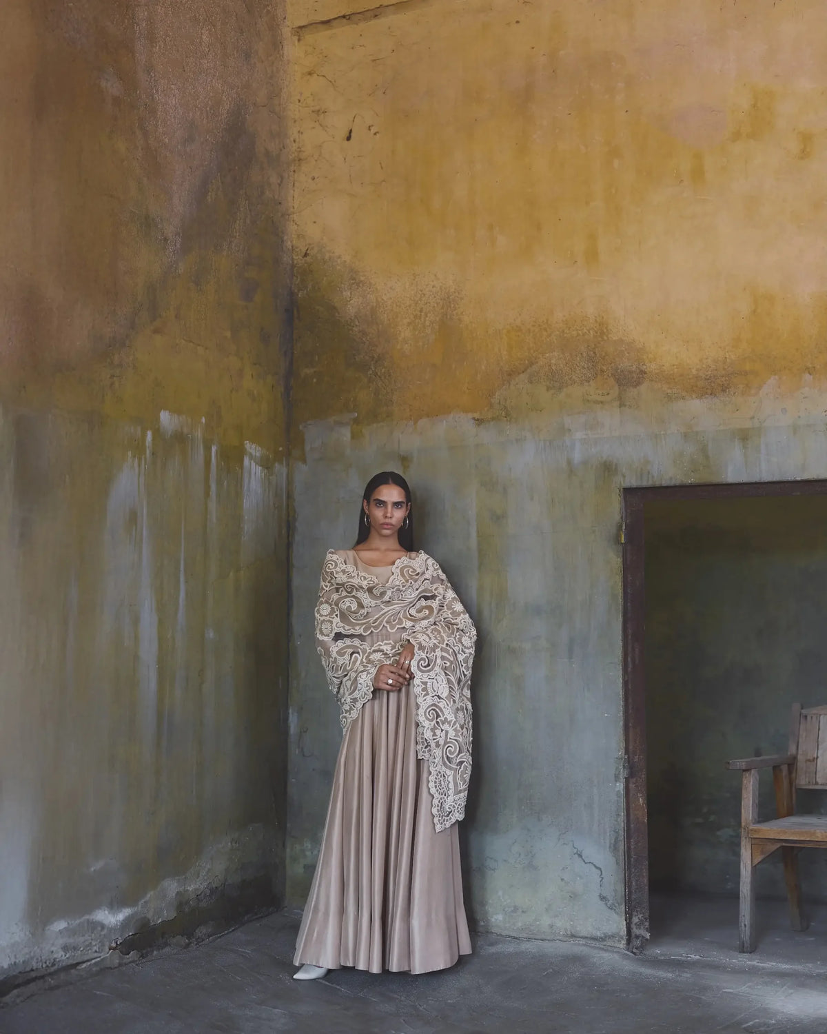 Woman in an ornate dress standing in a room with peeling walls.
