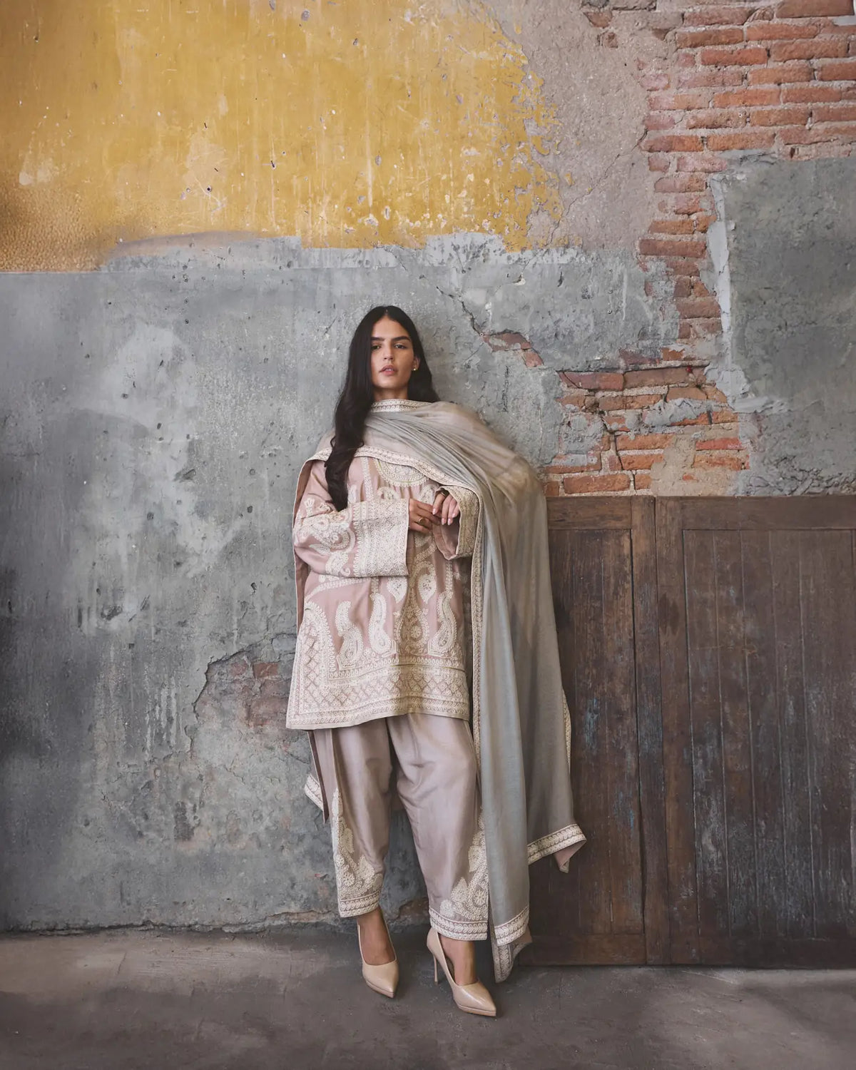 Woman in traditional outfit standing against a textured wall.