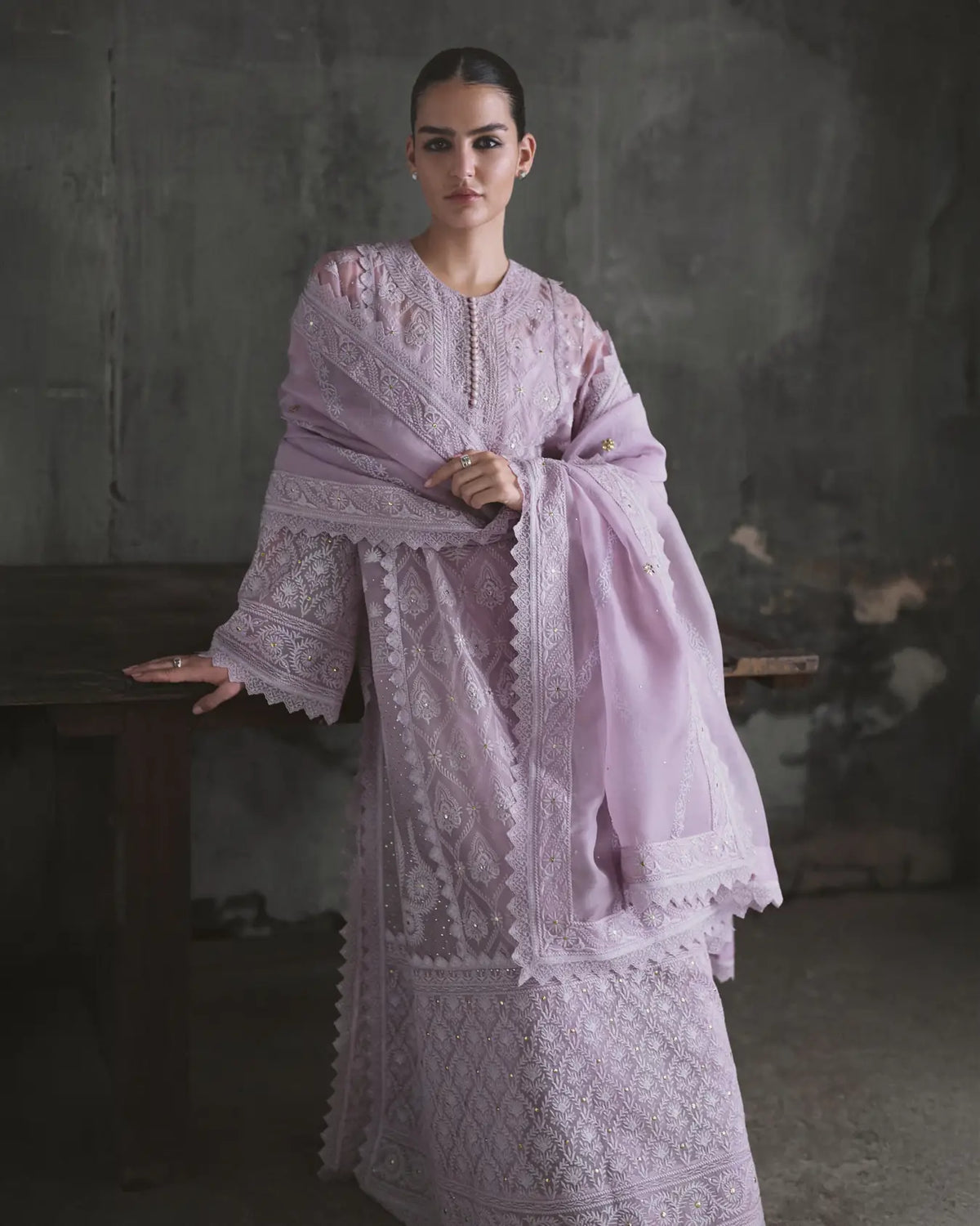 Woman wearing a light purple embroidered traditional outfit against a dark background