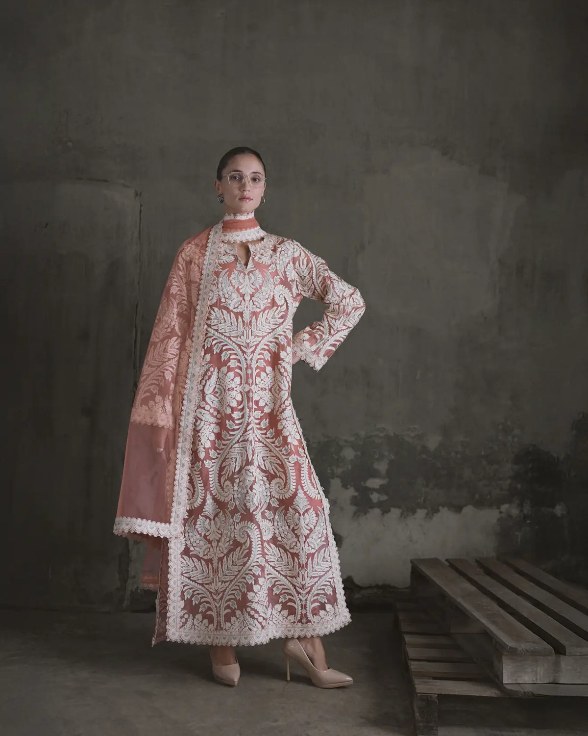 Woman wearing a traditional embroidered outfit against a textured wall.
