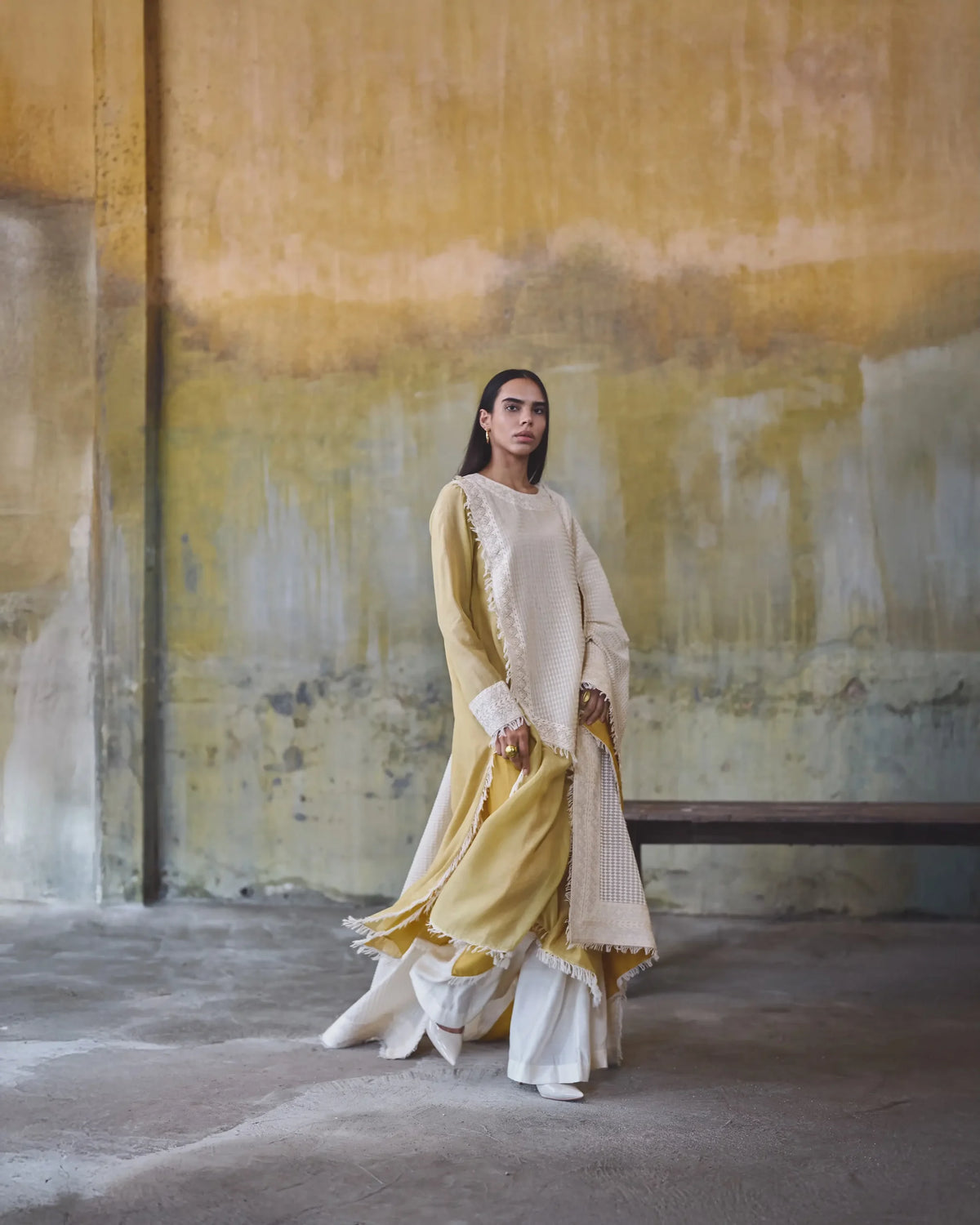Woman in a traditional outfit standing against an abstract wall.