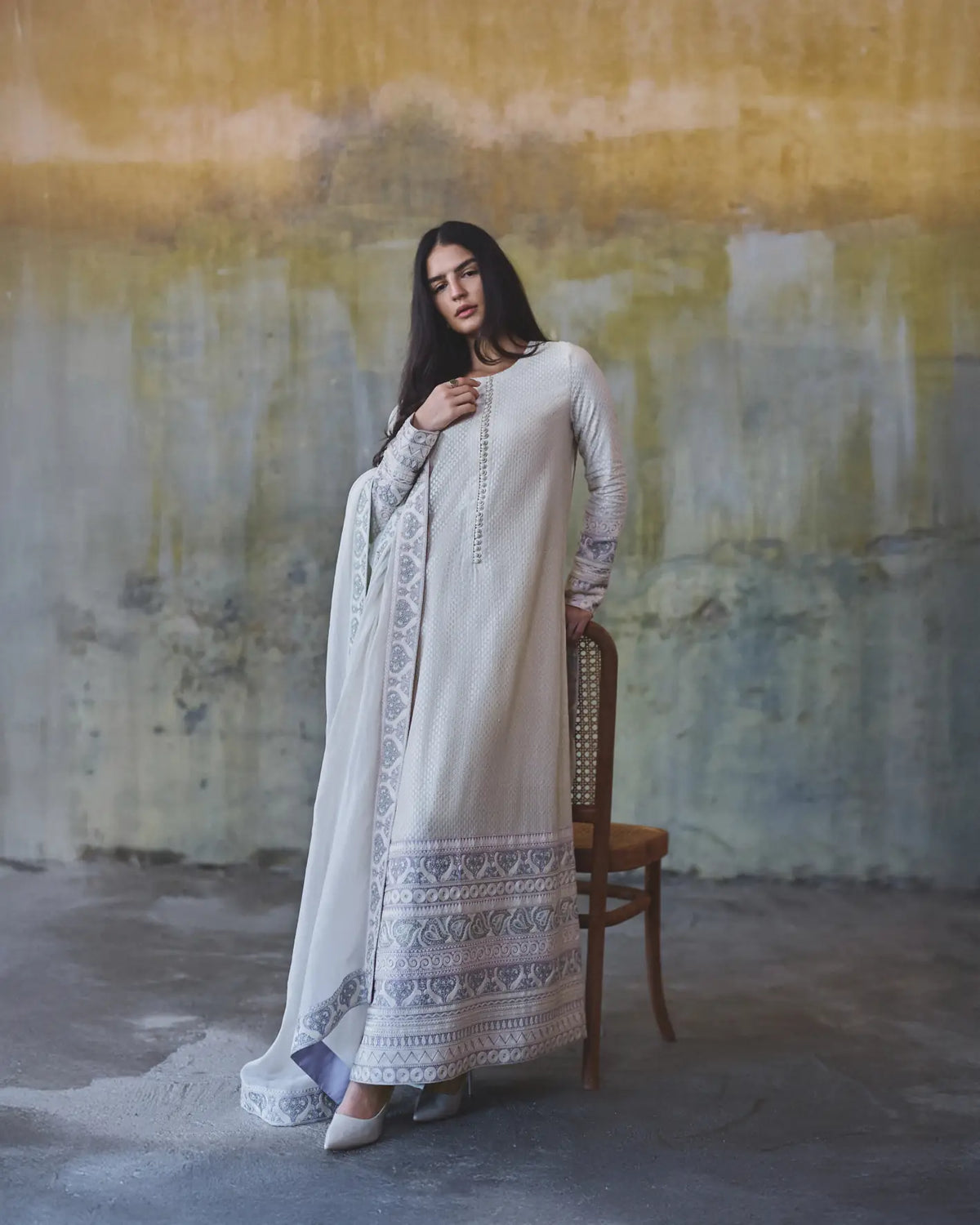 Woman in a white traditional outfit standing in front of an abstract wall painting.