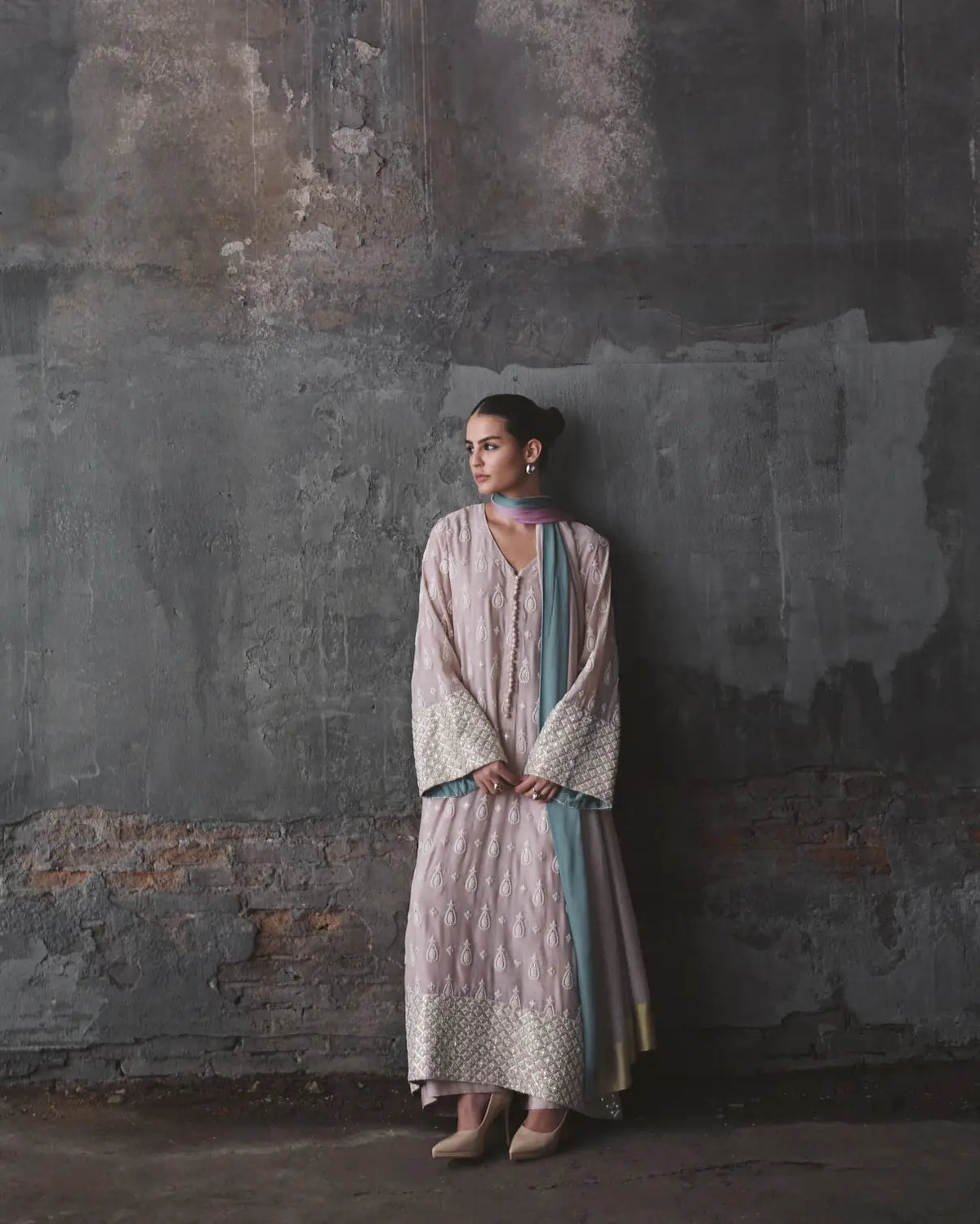 Woman in a traditional outfit standing against a textured wall.