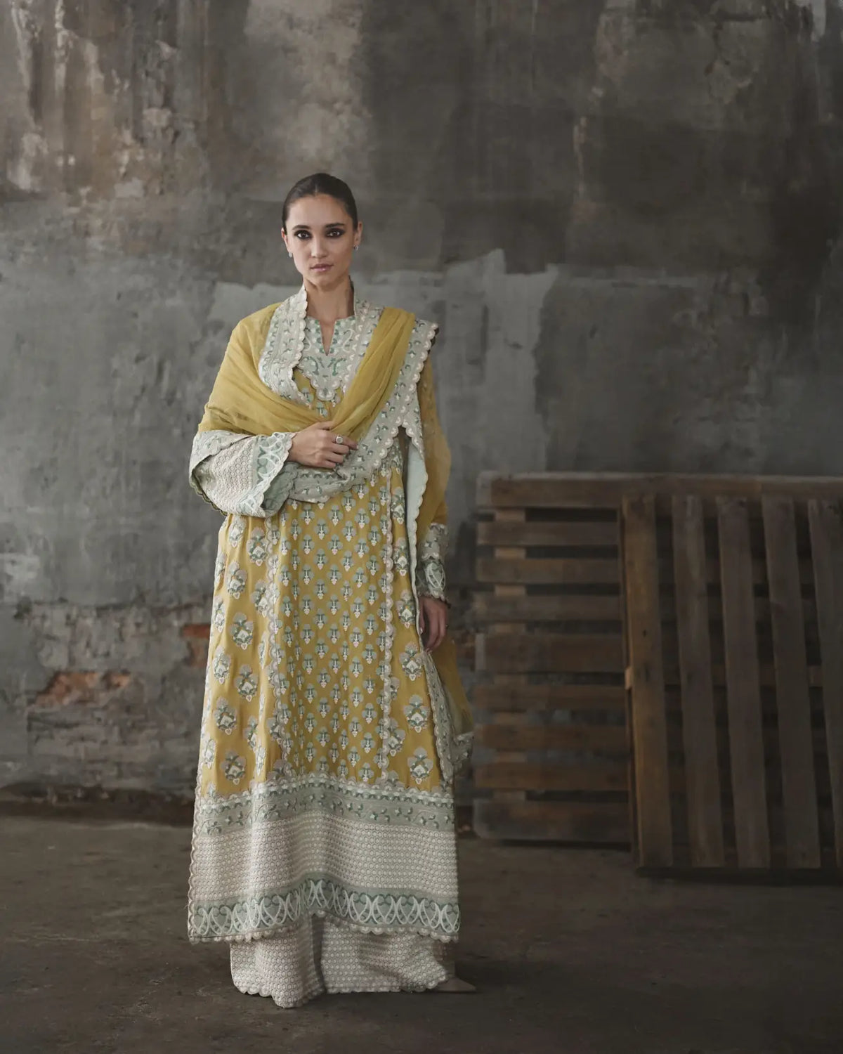 Woman in a traditional outfit standing against a rustic wall.