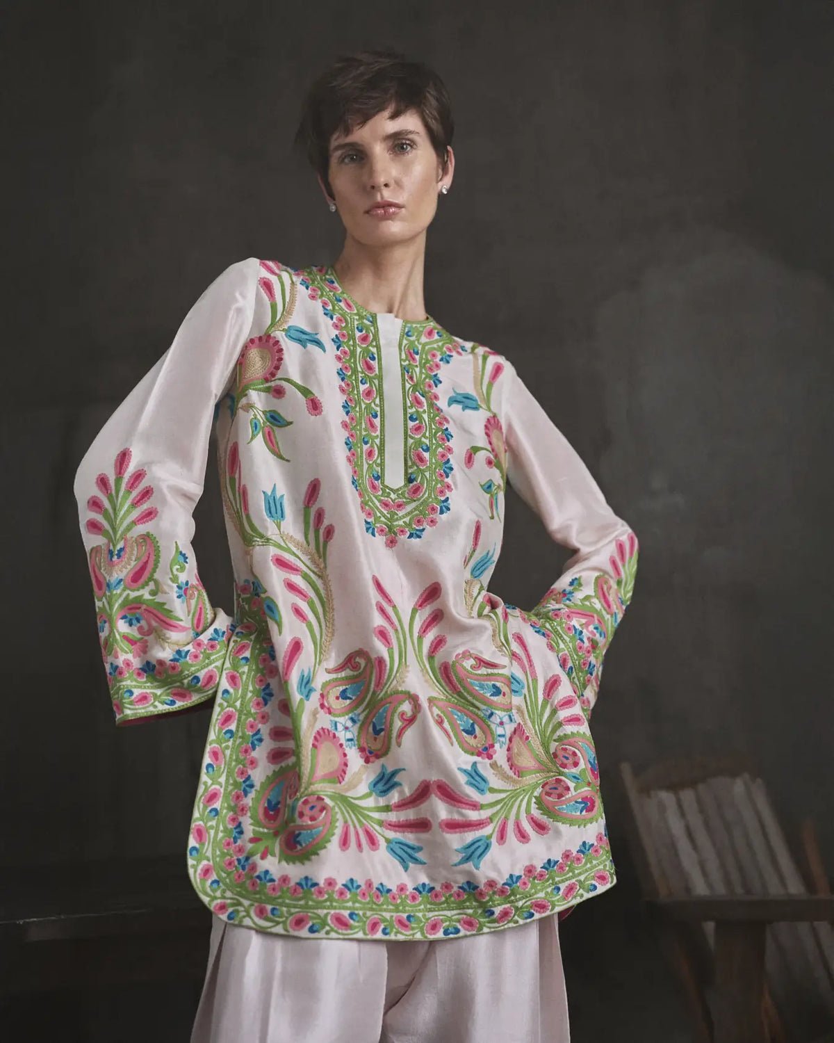 Woman wearing a white embroidered top with colorful patterns against a dark background