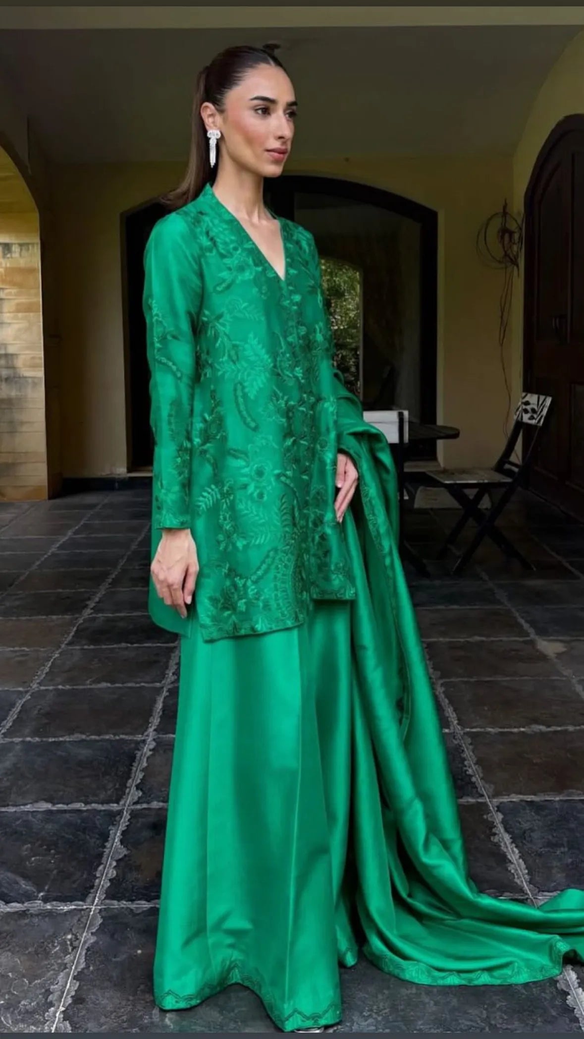 Woman in a green embroidered outfit standing on a stone floor.