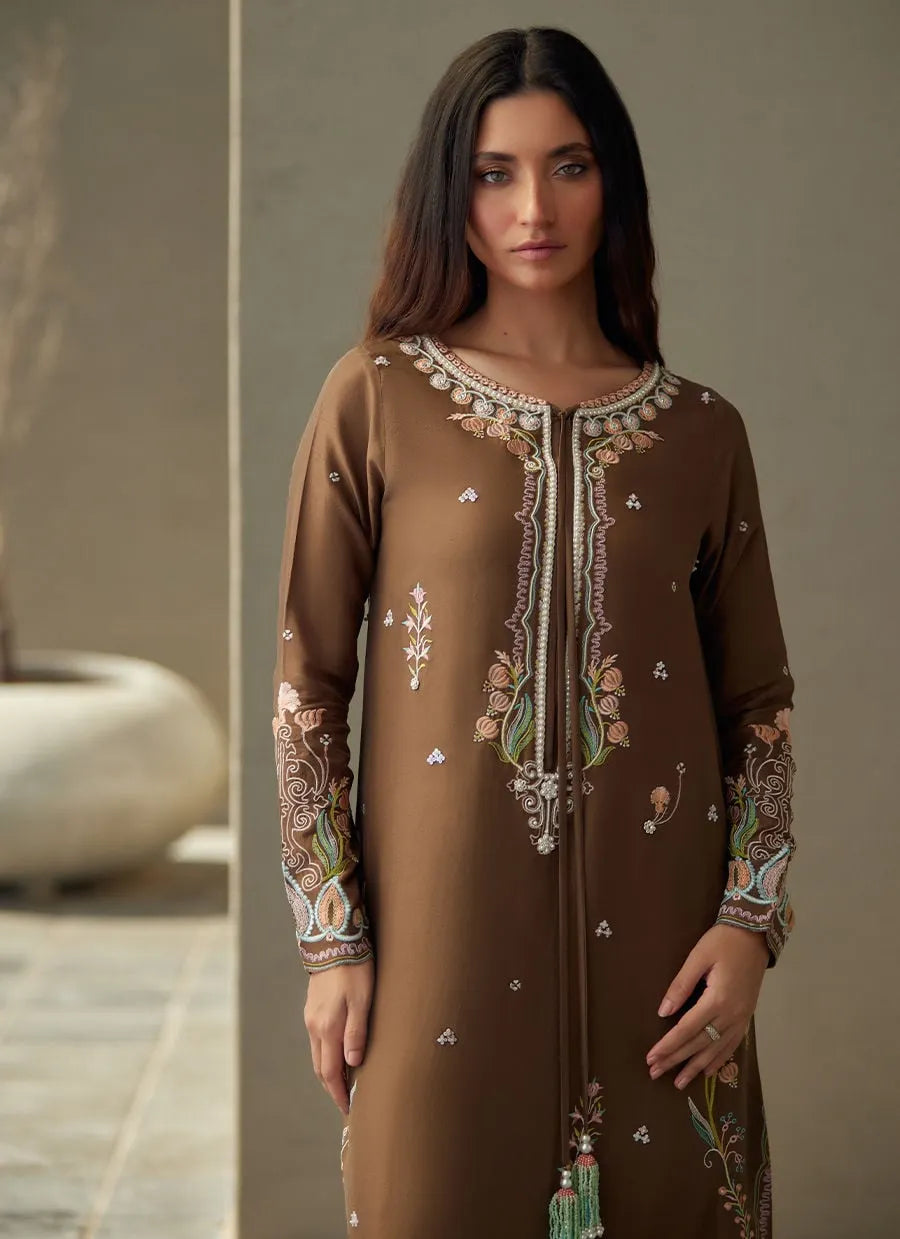 Woman wearing a brown embroidered dress with tassels against a neutral background