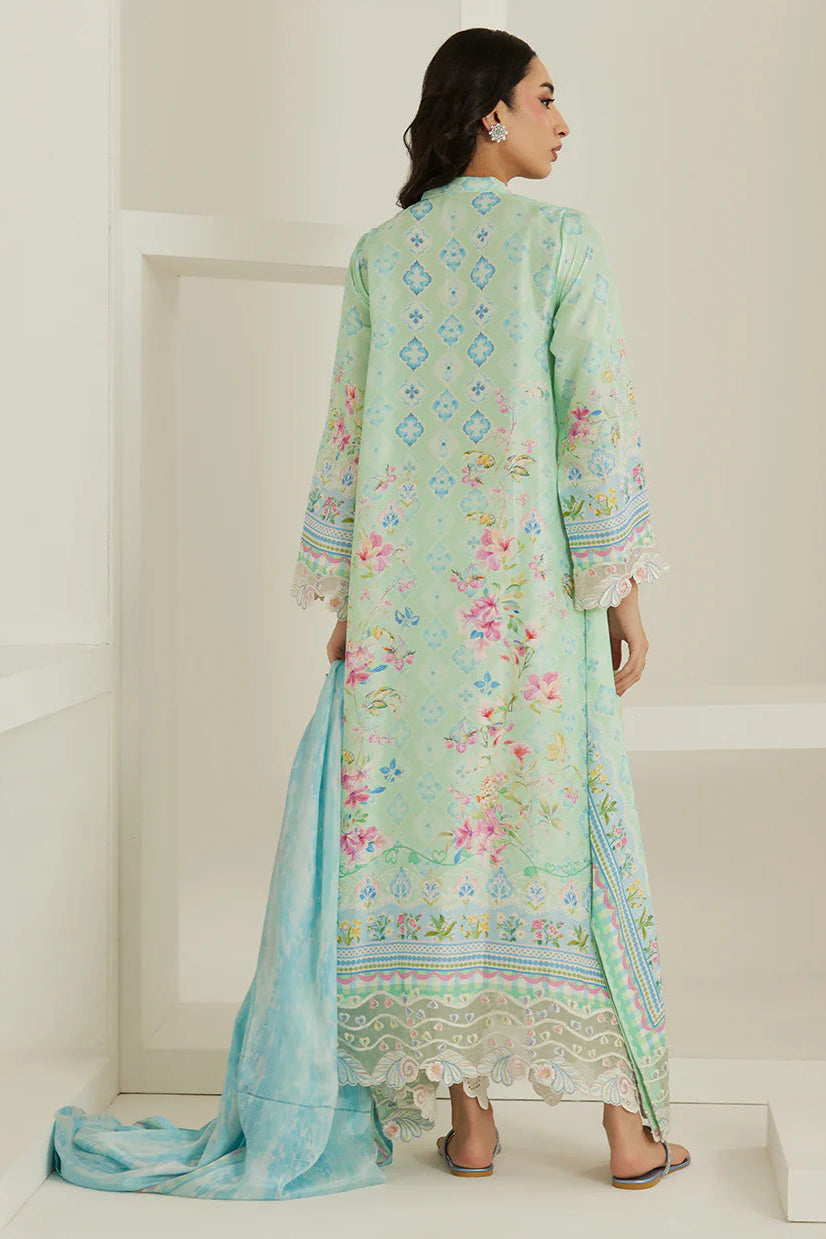 Woman wearing a light green and blue embroidered traditional outfit in a minimal white room.