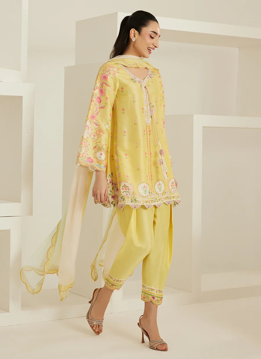 Woman wearing a yellow embroidered outfit with a sheer dupatta in a minimalistic setting