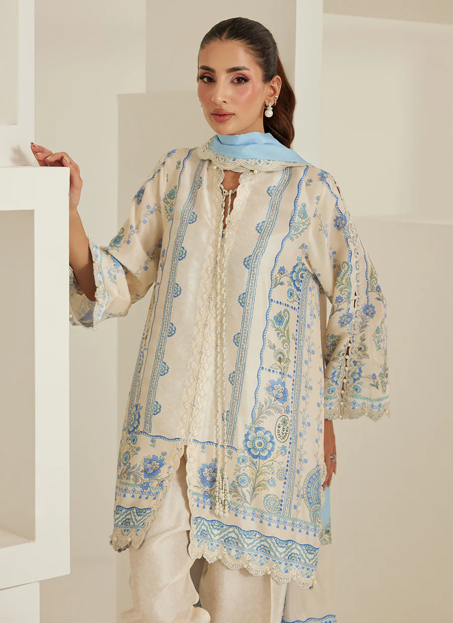 Woman wearing a cream and blue embroidered traditional outfit in a minimalistic setting