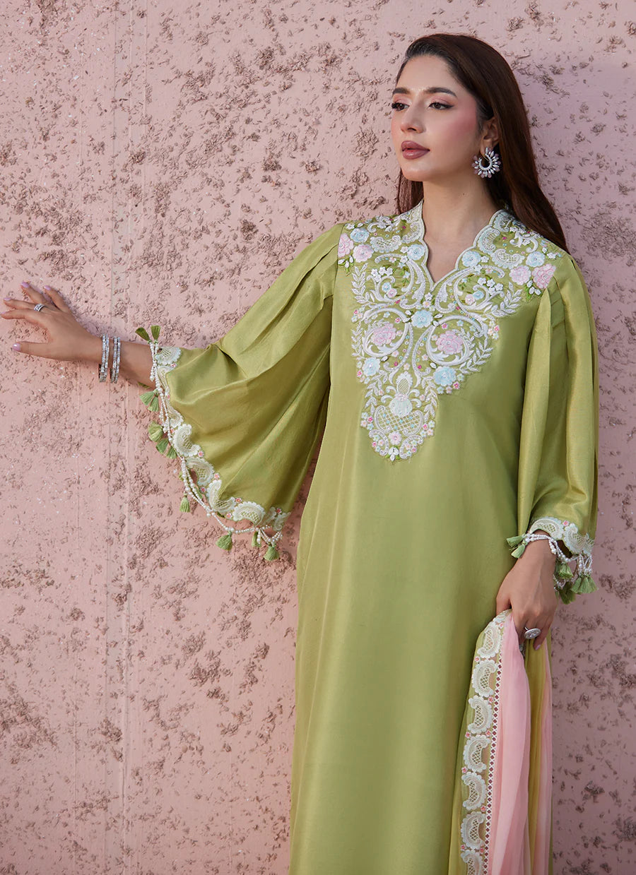 Woman wearing a green embroidered dress with a pink scarf against a textured pink wall.