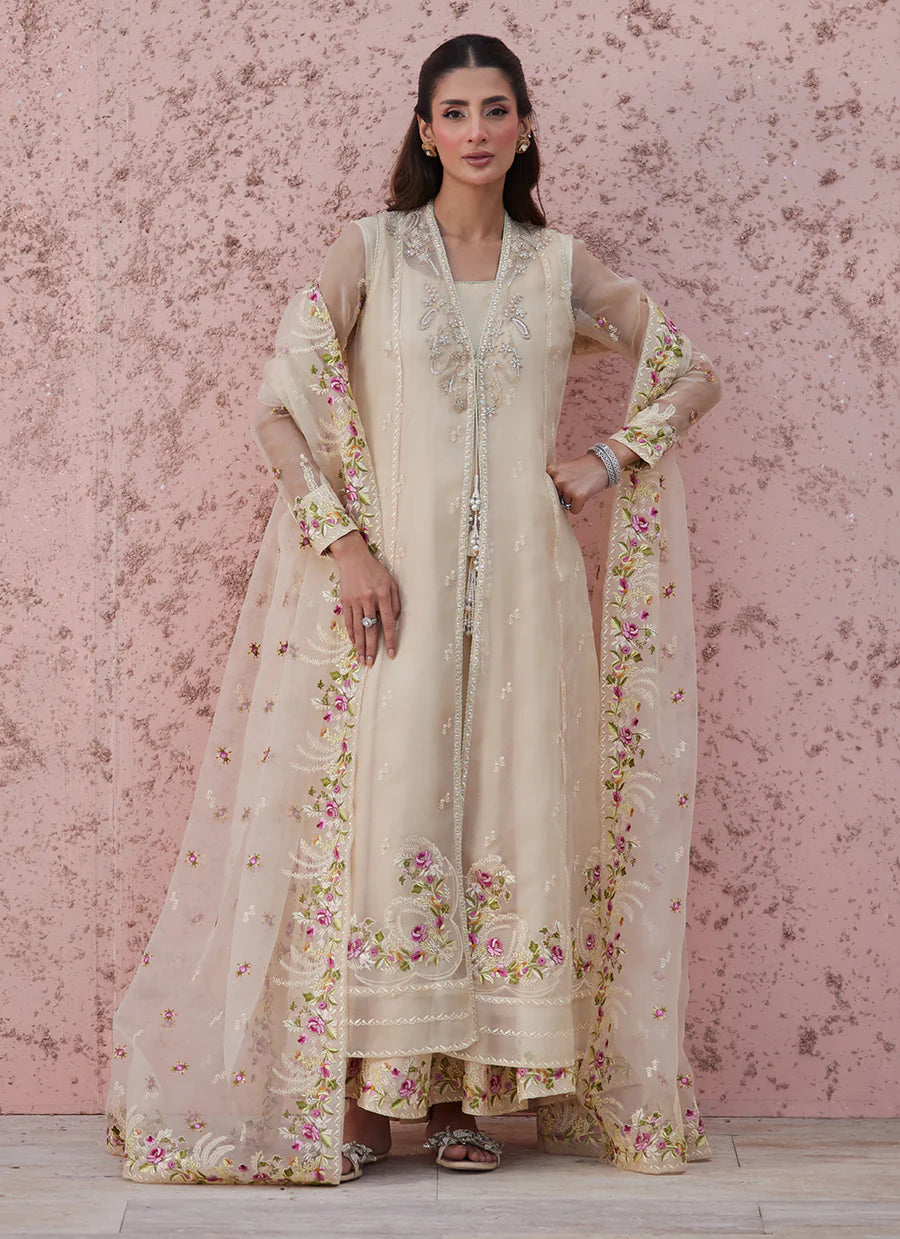 Woman wearing a cream-colored traditional outfit with floral patterns against a pink floral background