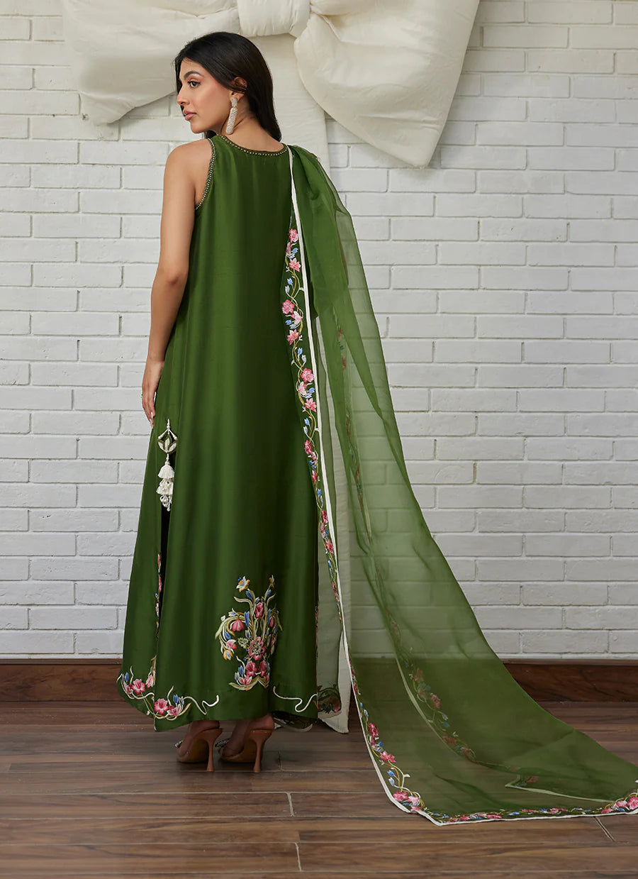 Woman wearing a green embroidered outfit with a matching dupatta against a white brick wall.