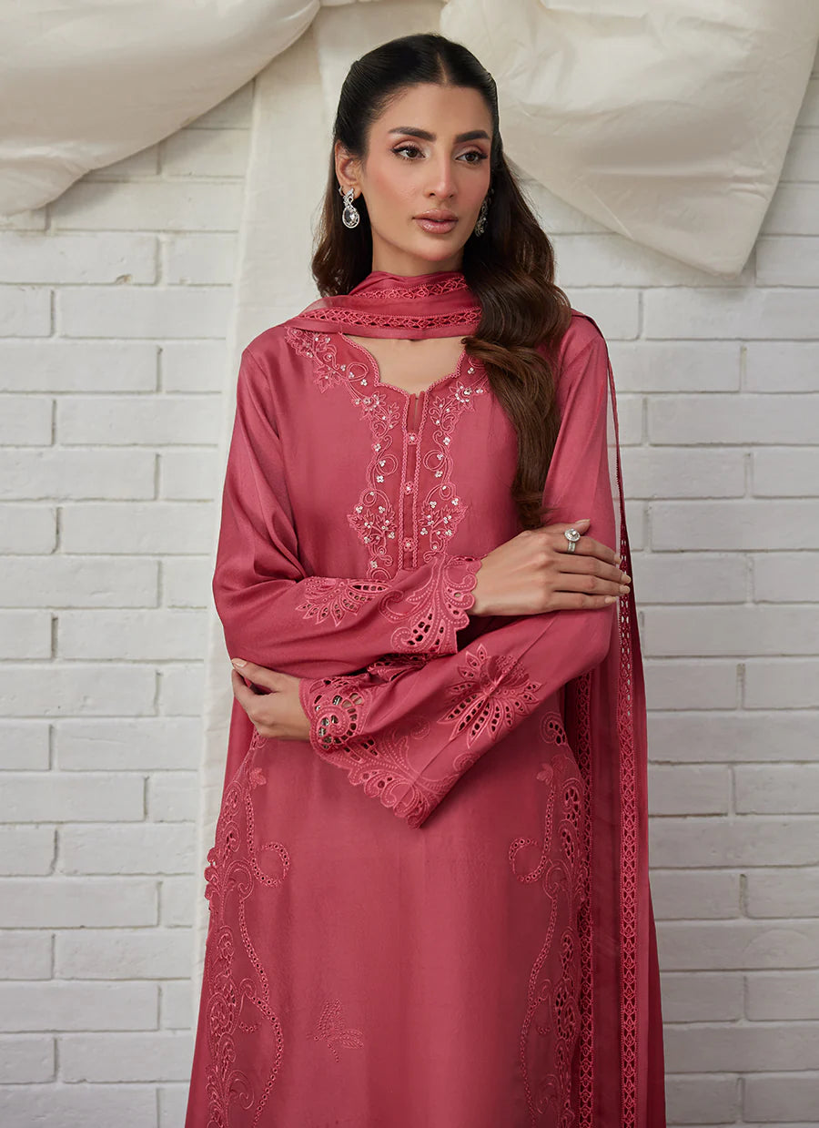 Woman wearing a pink embroidered traditional outfit against a white brick wall.