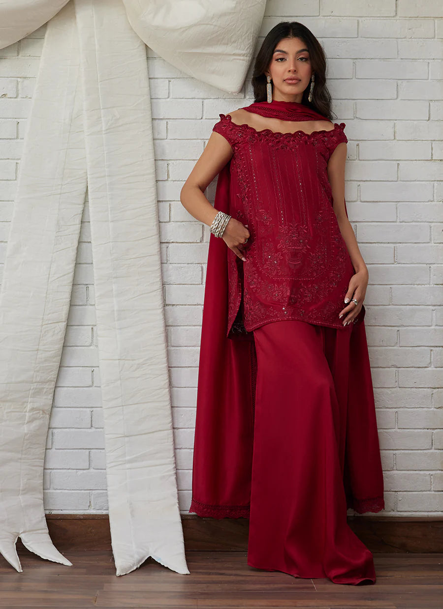 Woman in a red outfit standing against a white brick wall with draped fabric.