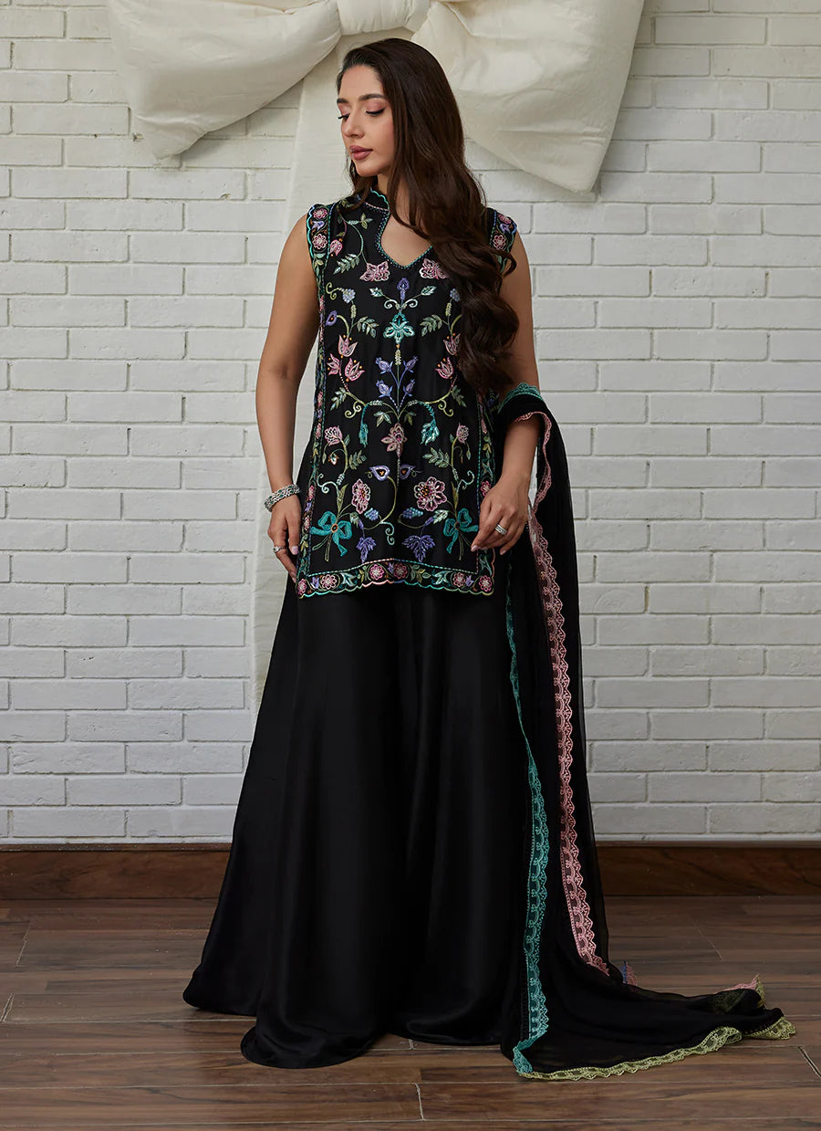 Woman wearing a black embroidered outfit with a white brick wall background