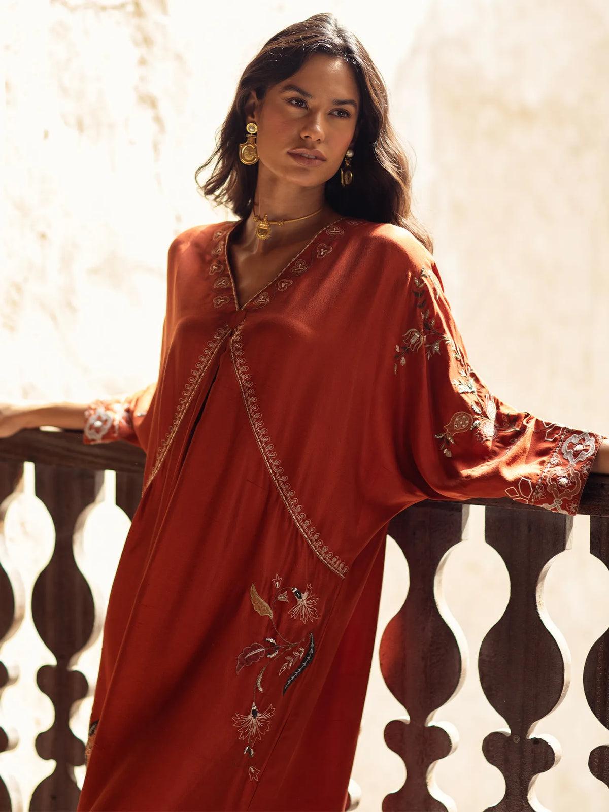 Woman wearing a red embroidered dress leaning against a decorative railing.