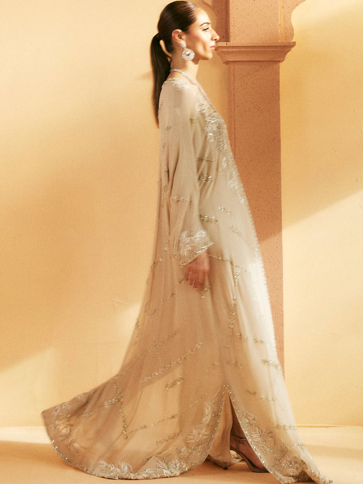 Woman wearing a light-colored embroidered outfit against a beige background