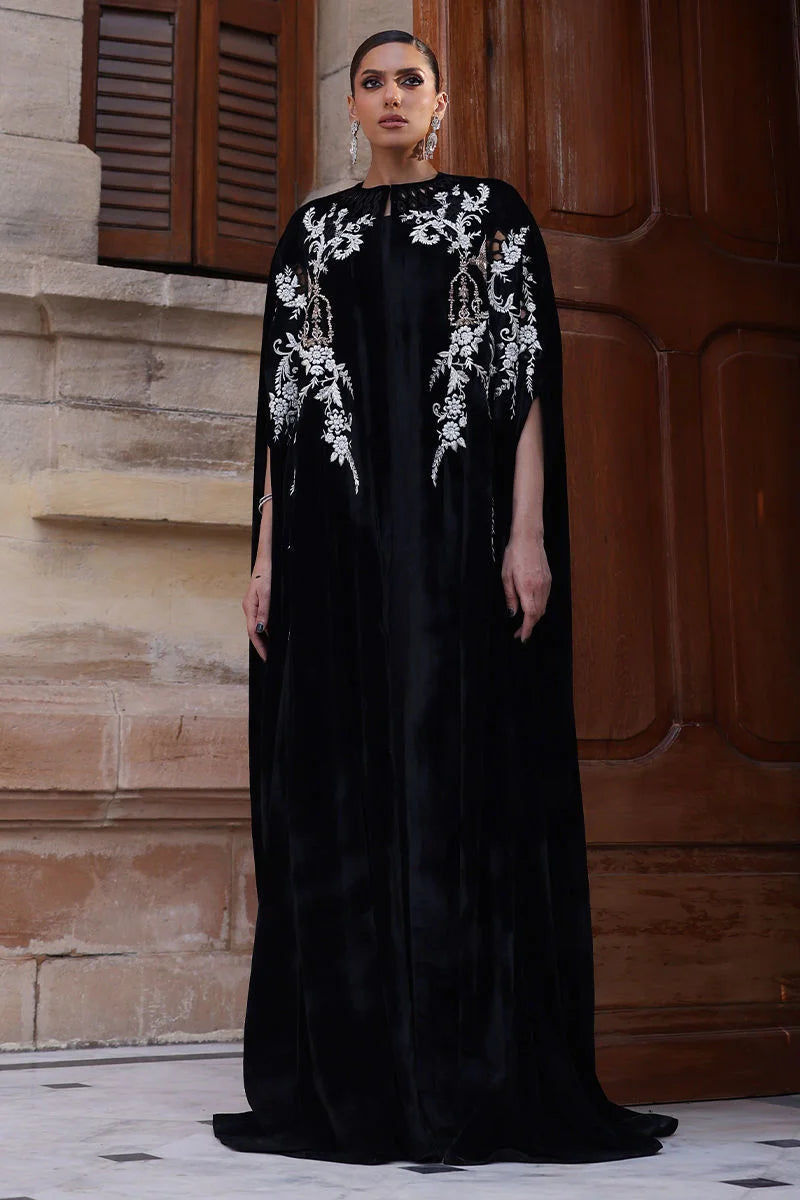 Woman wearing a black dress with white embroidery standing in front of a stone wall.