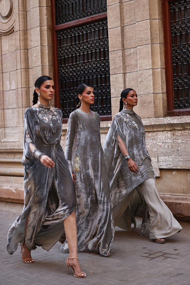 Three women in silver dresses standing in front of a building entrance.