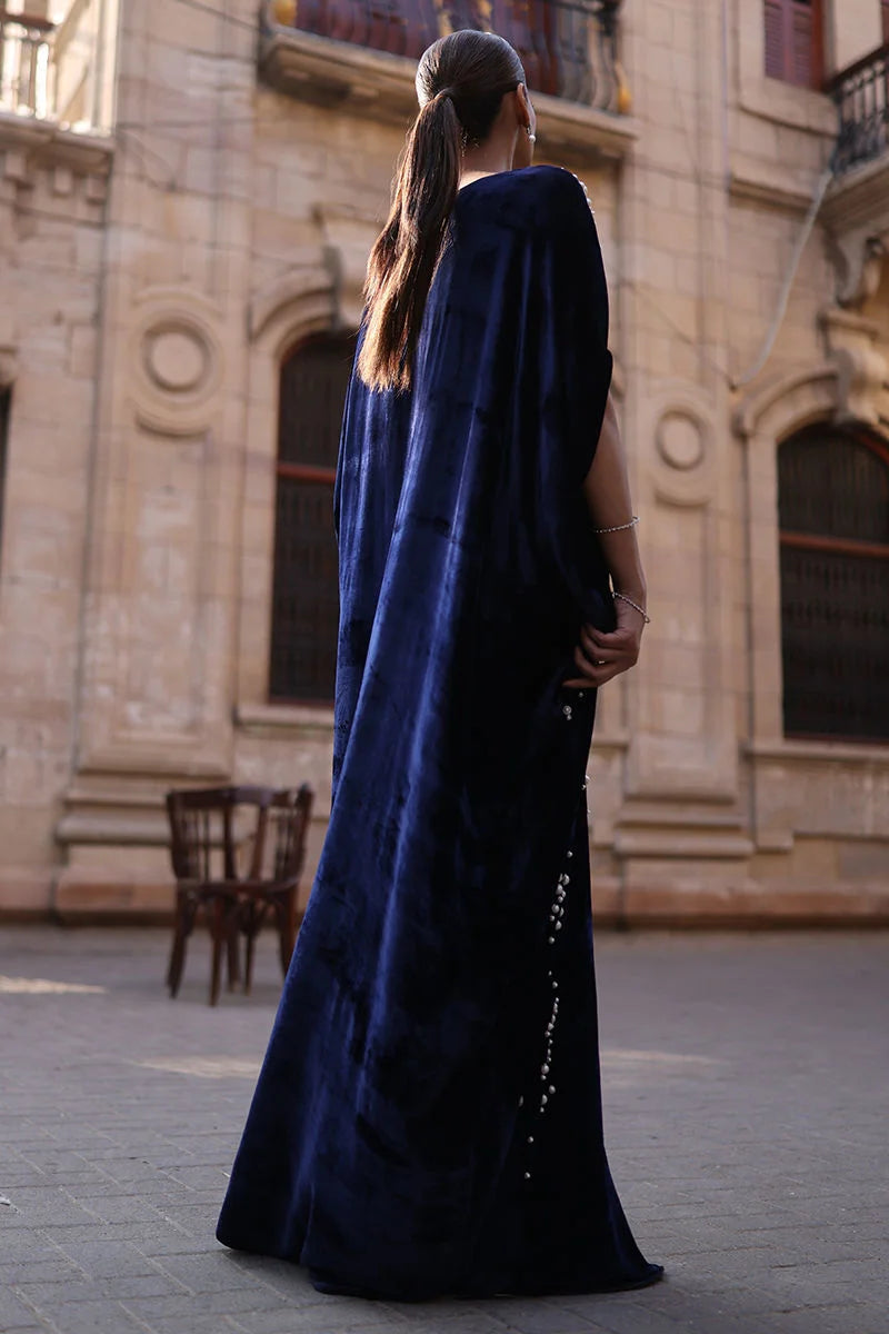 Person wearing a long blue dress standing in front of an architectural building.
