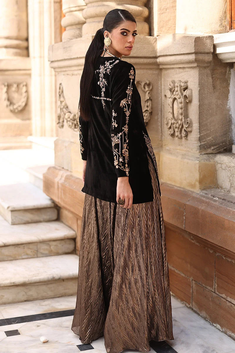 Woman in black and gold traditional outfit standing on stone steps.
