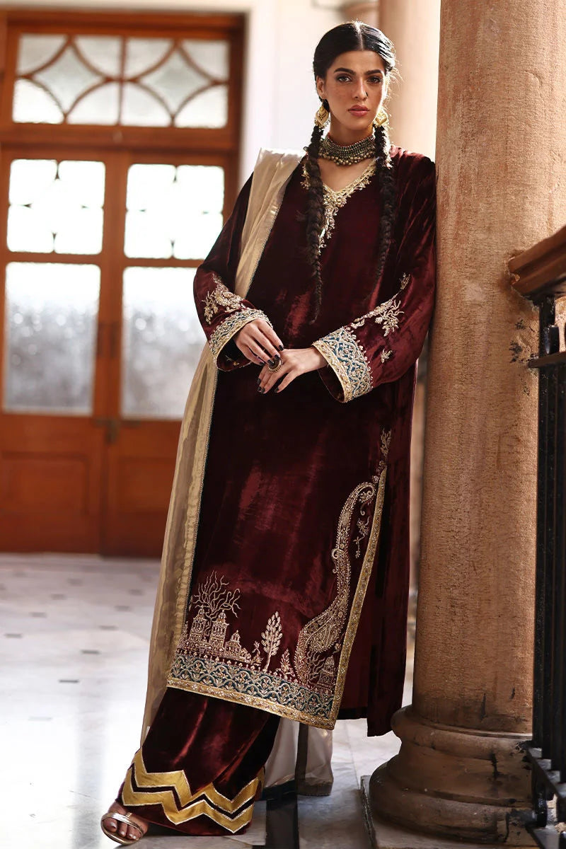 Woman in a traditional maroon and gold outfit standing indoors.